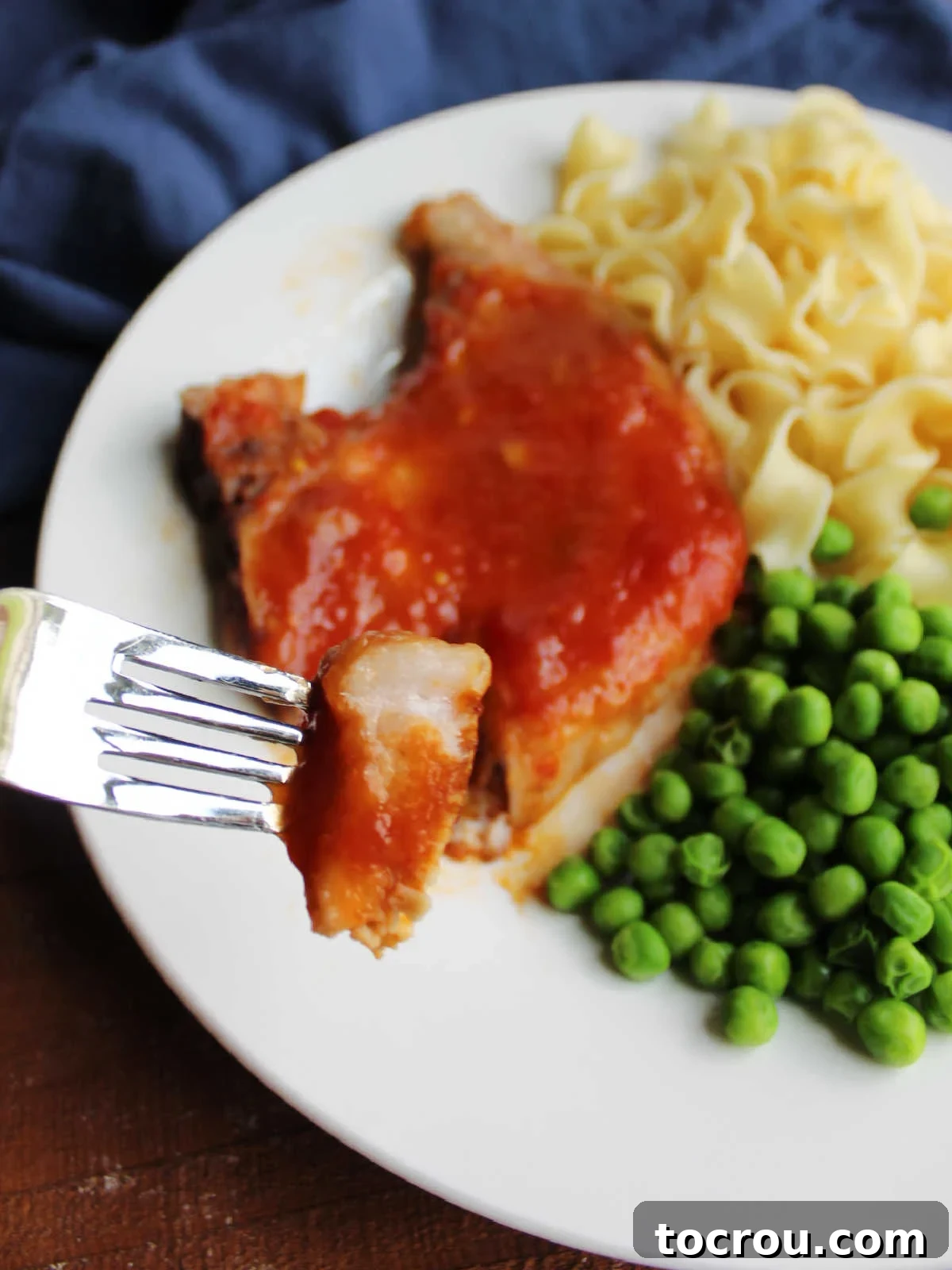 Bite of sweet and sour pork chop on fork, showing tender inside and thick tomato based sauce on the outside. 