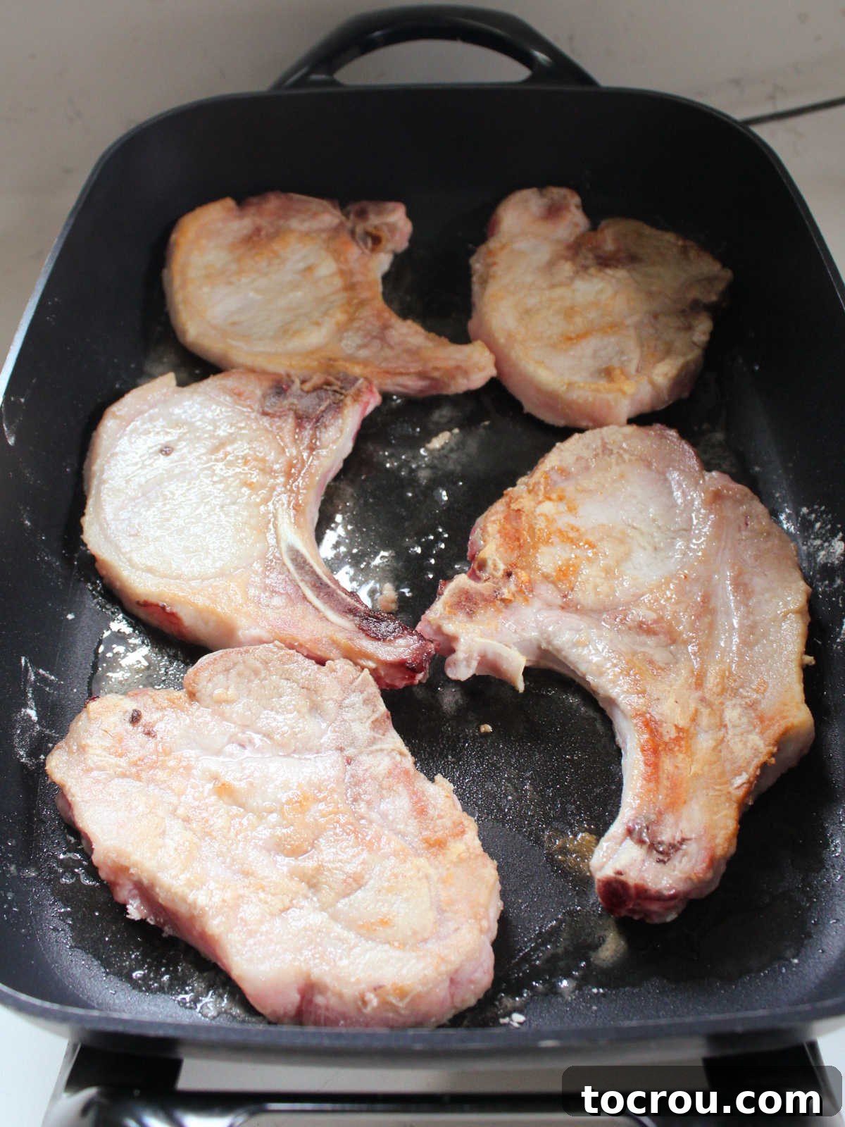 Browned pork chops in a large electric skillet.