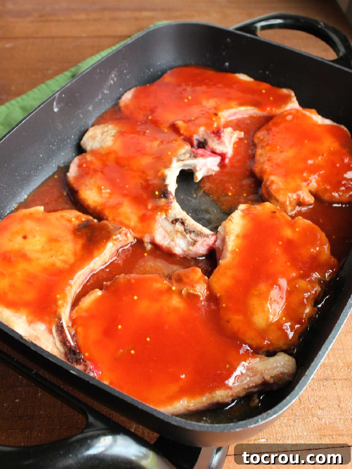 Ketchup and pickle juice sauce poured over browned pork chips in electric skillet, ready to simmer. 