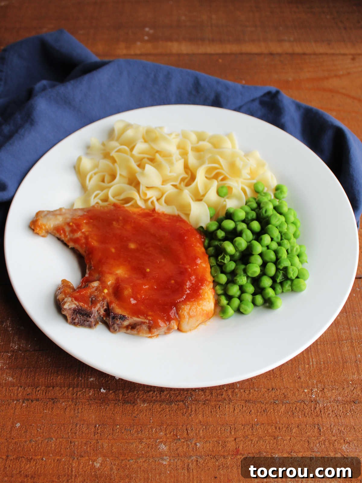 Dinner plate of pork chop with sweet and sour sauce served with peas and pasta. 