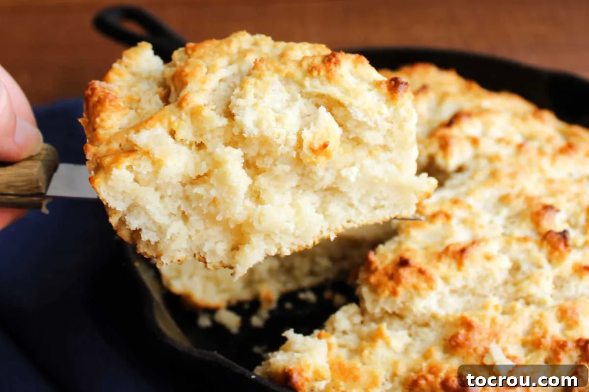 Spatula lifting first slice of pone bread out of cast iron skillet showing soft interior and golden brown crust.