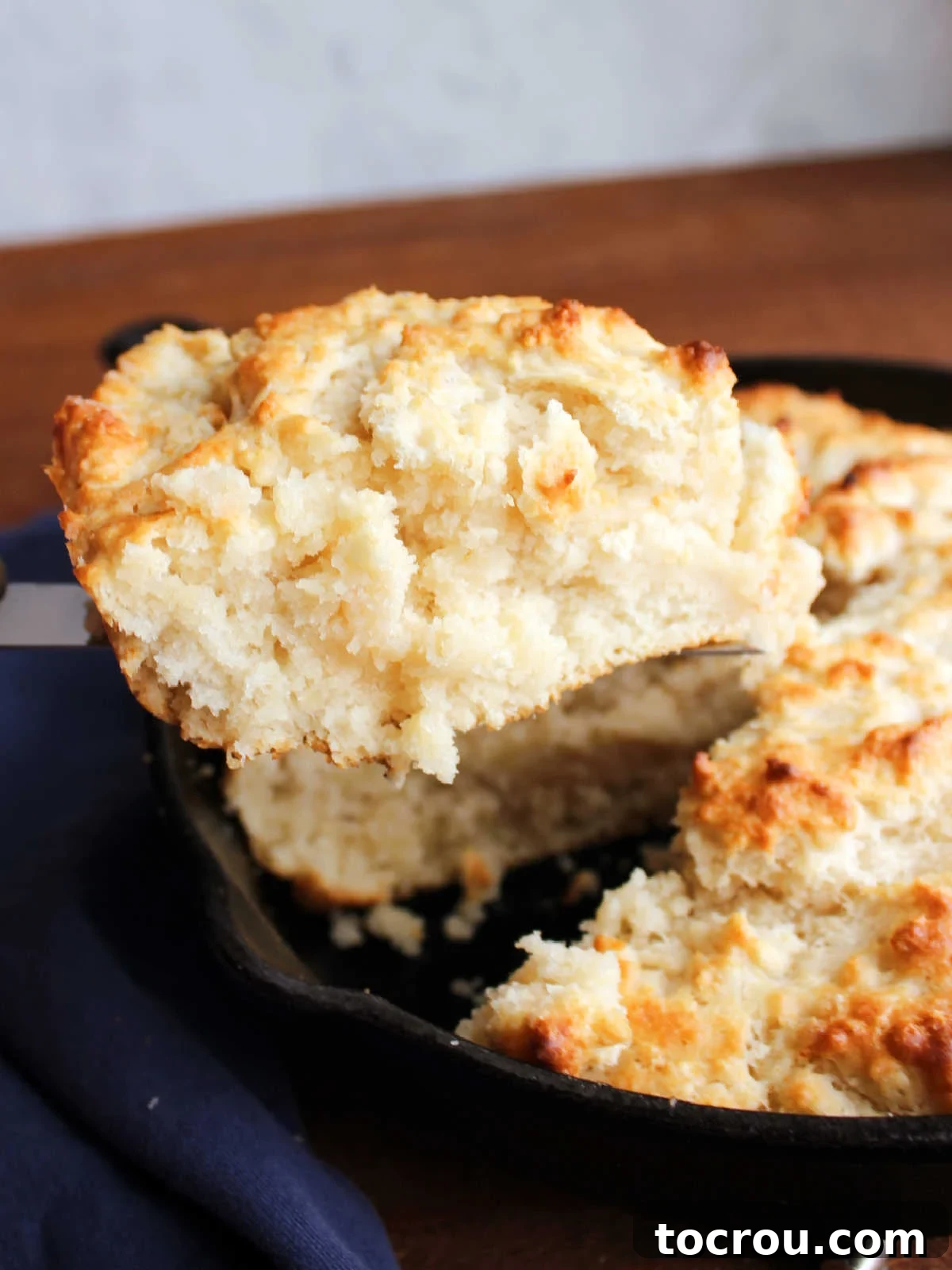 Spatula lifting out first slice of pone bread showing soft biscuit like texture on the inside and golden brown top.