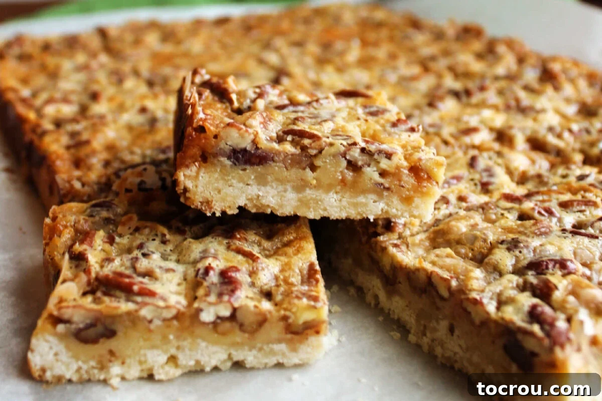 Squares of pecan pie bars neatly arranged on a parchment-lined cutting board, showcasing the distinct layers of the golden shortbread crust and the rich, shimmering pecan filling, topped with toasted pecan pieces.