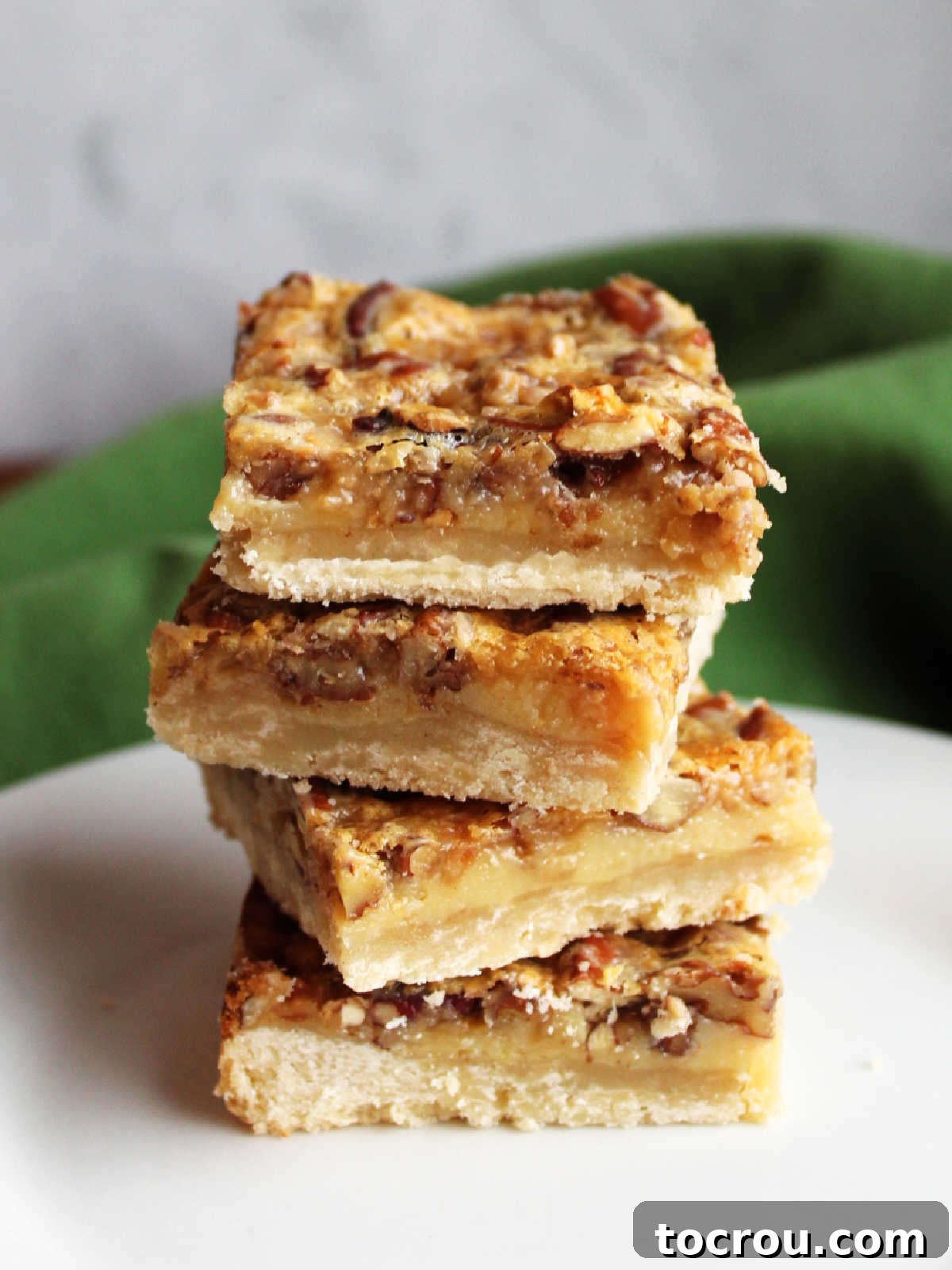 A visually appealing stack of four perfectly cut pecan pie bars, clearly displaying the distinct layers of the crumbly shortbread crust and the thick, rich, and gooey pecan filling. The image emphasizes their sturdy nature and attractive form.