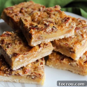 Pecan pie bars stacked enticingly on a white plate, revealing their multi-layered goodness with a crisp shortbread crust and a rich, gooey pecan filling.