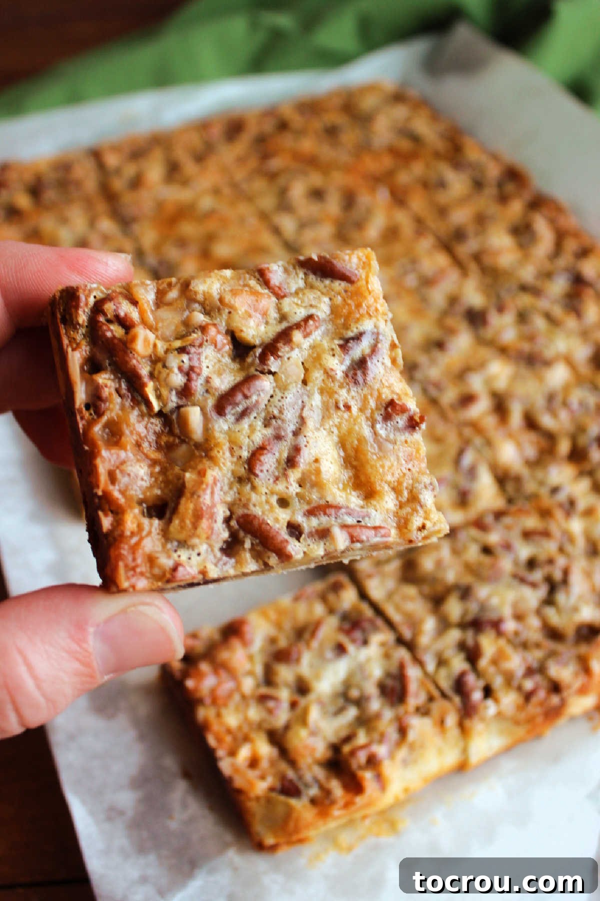 A hand gently holding a single pecan pie bar square, highlighting its beautiful golden brown top and robust structure, demonstrating its perfect handheld quality.