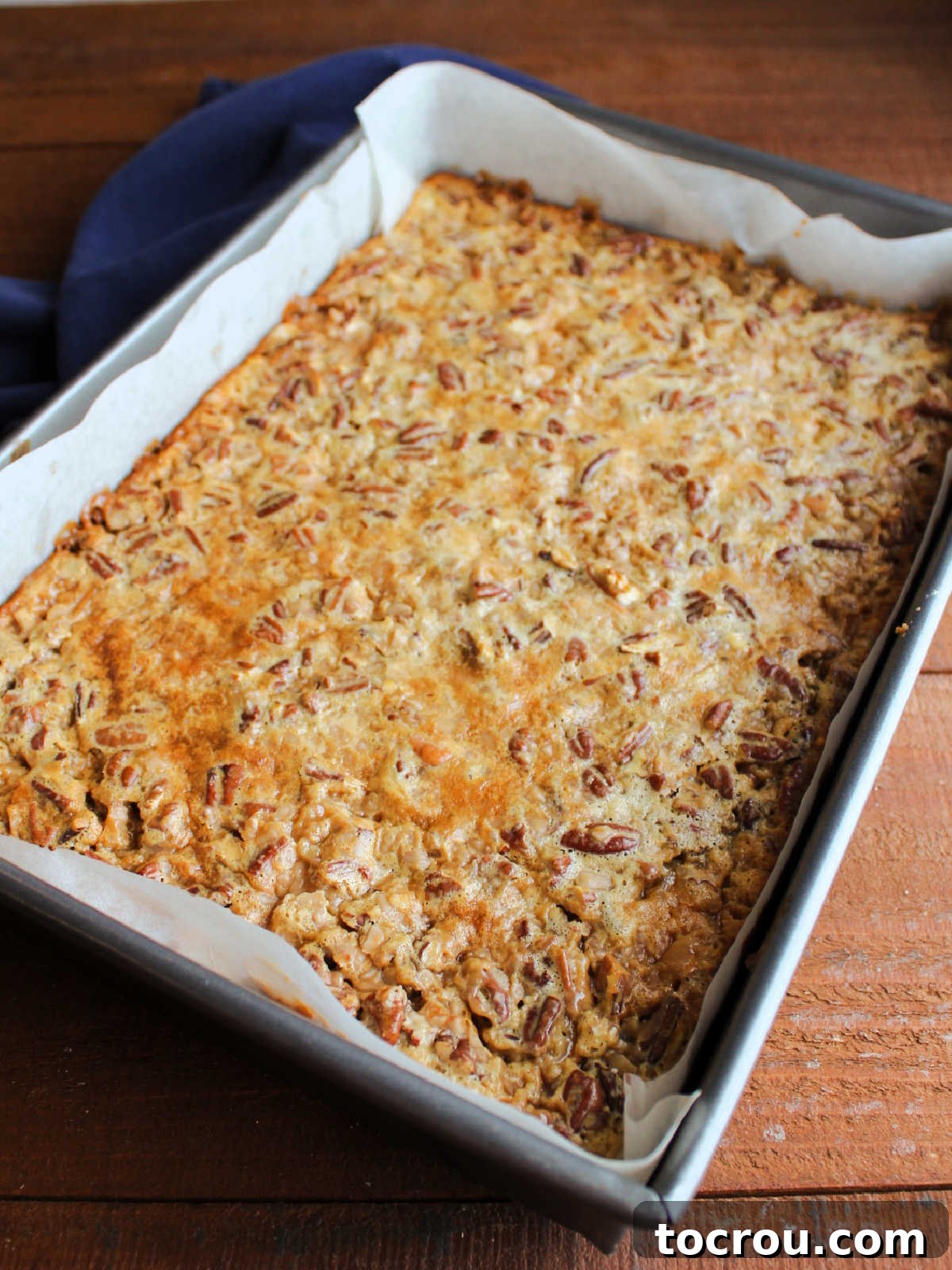 Freshly baked pecan pie bars cooling in the pan, displaying the beautiful golden brown and bubbly surface of the pecan filling after achieving perfect doneness in the oven.