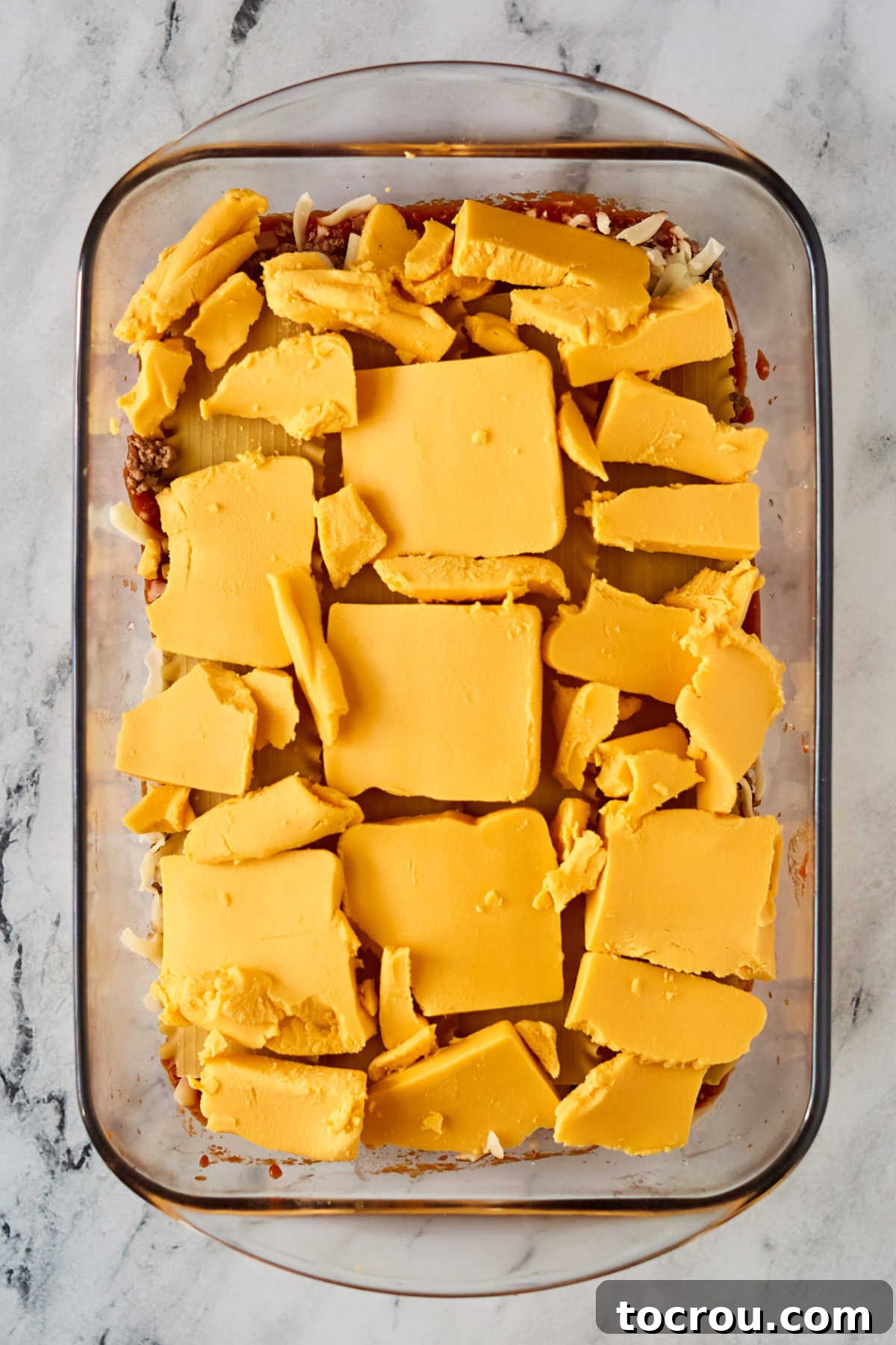 Velveeta Cheese Layer in Lasagna The crucial middle layer of lasagna featuring neatly arranged slices of Velveeta cheese covering a bed of pasta, poised for the subsequent layers of sauce and meat, illustrating the unique cheesy core of the recipe and promising ultimate creaminess.