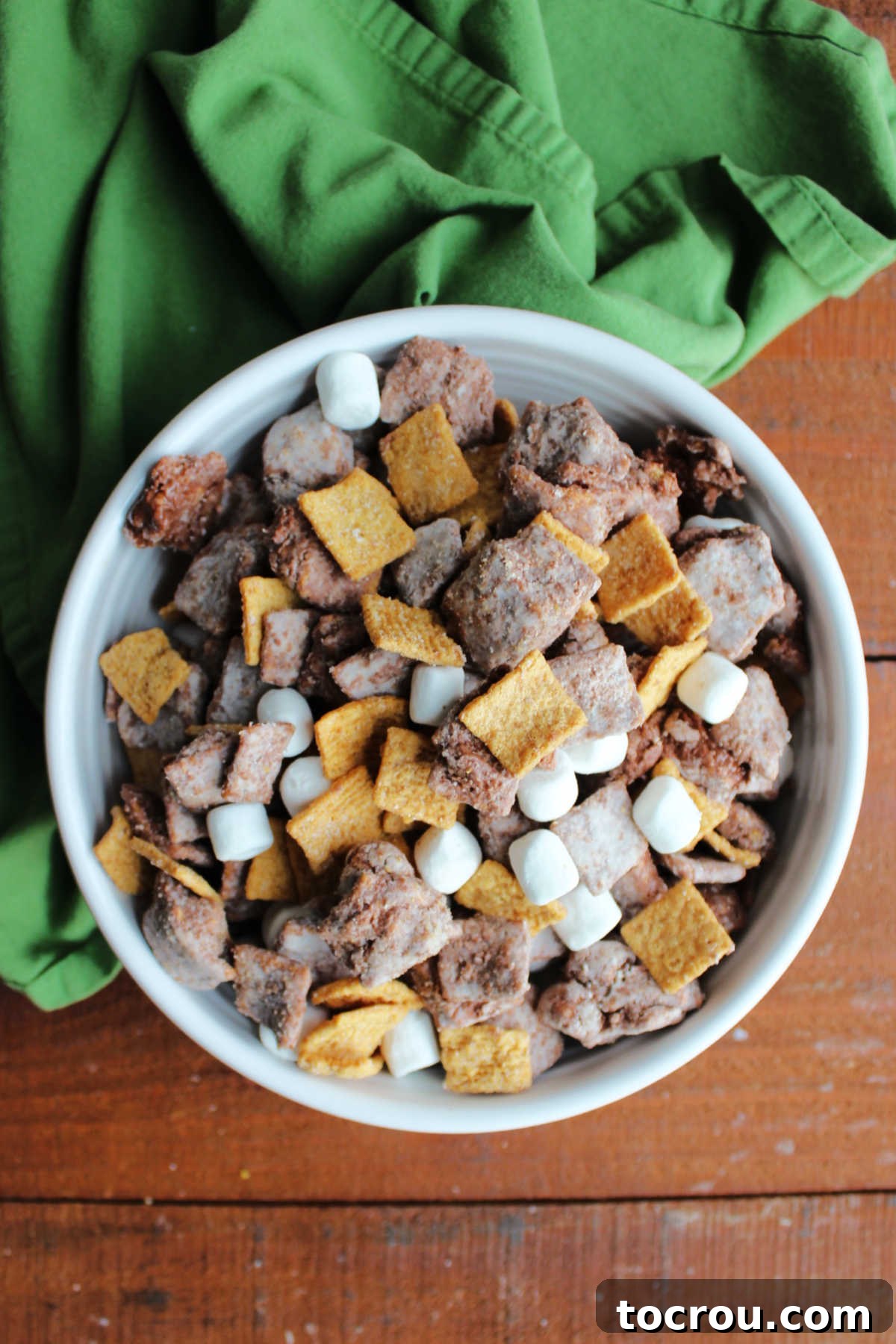 Bowl of puppy chow with graham cereal coated in chocolate and powdered sugar with mini marshmallows, ready to eat.