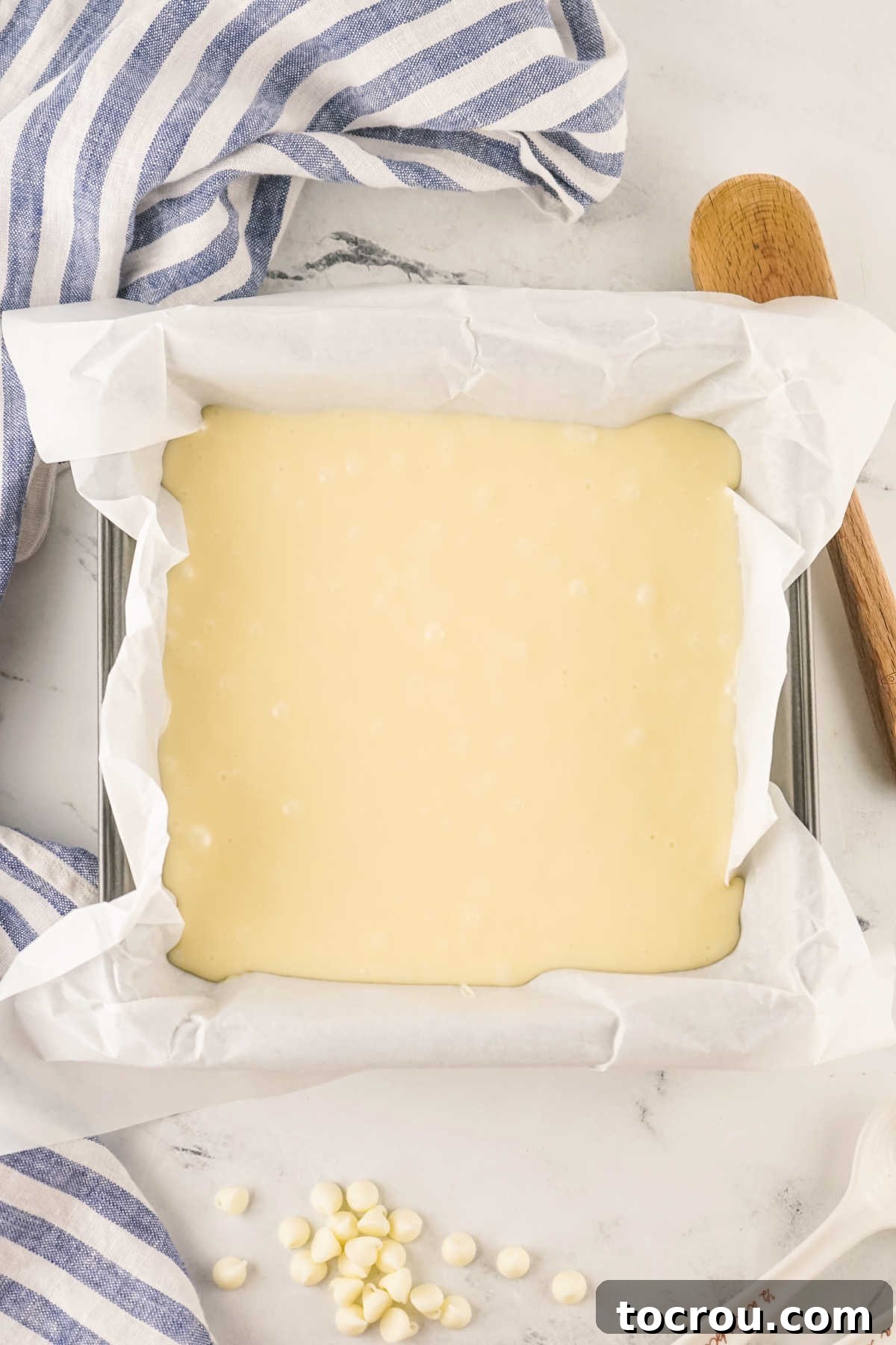A square baking pan, meticulously lined with parchment paper, is filled with the creamy, smooth vanilla fudge mixture, ready for chilling.
