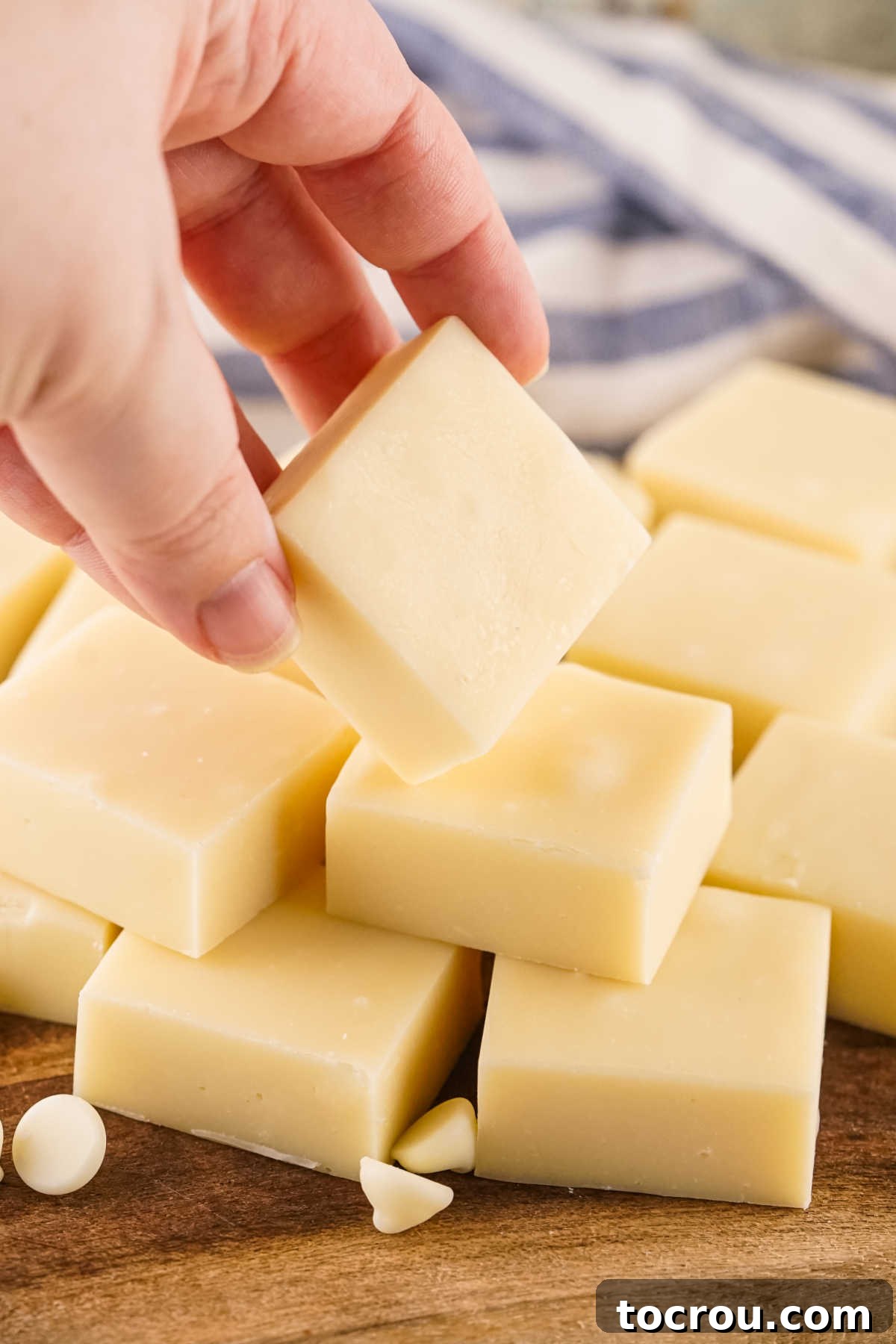 A hand gently holds a piece of smooth, cream-colored vanilla fudge, highlighting its inviting texture and readiness to be savored.