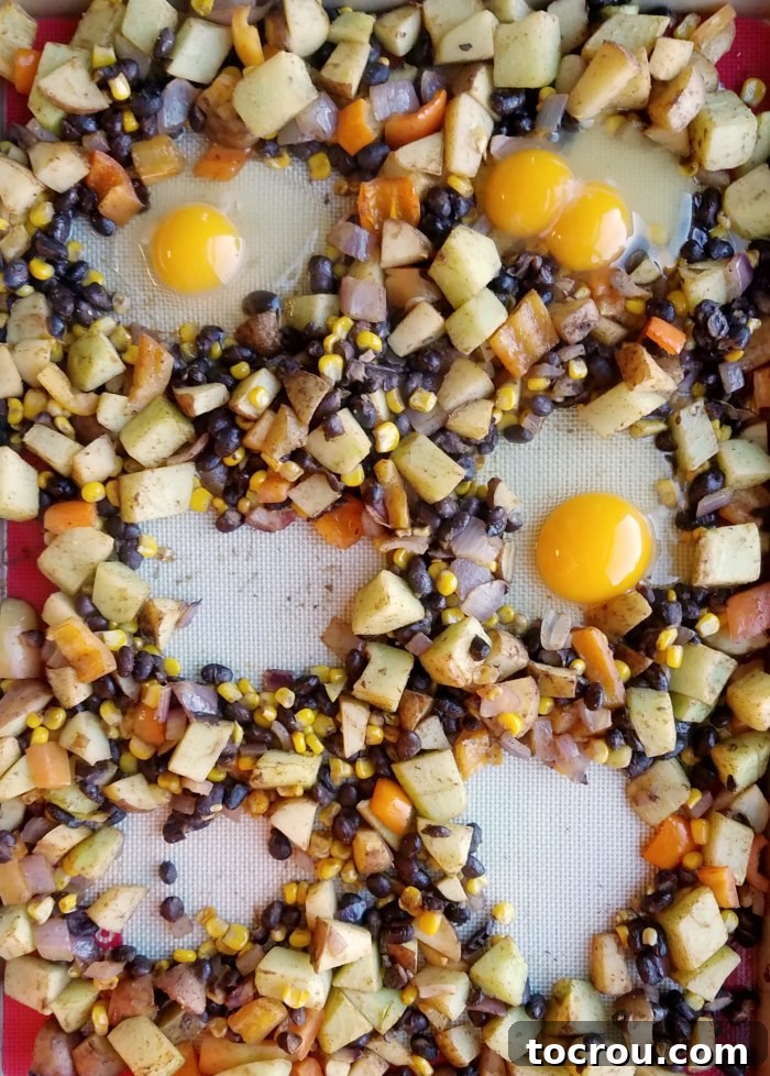 Sheet Pan Fiesta Breakfast 5 Eggs being cracked into nests formed by roasted veggies on sheet pan.