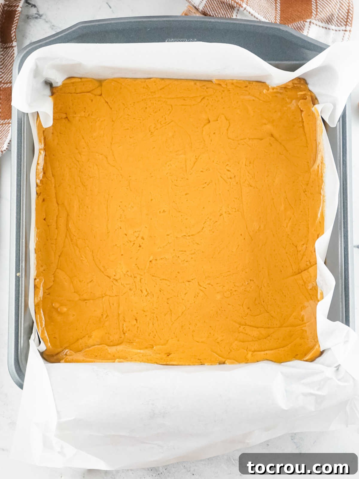 Caramel Fudge Setting in Lined Pan Square baking dish lined with parchment paper and filled with caramel fudge mixture.