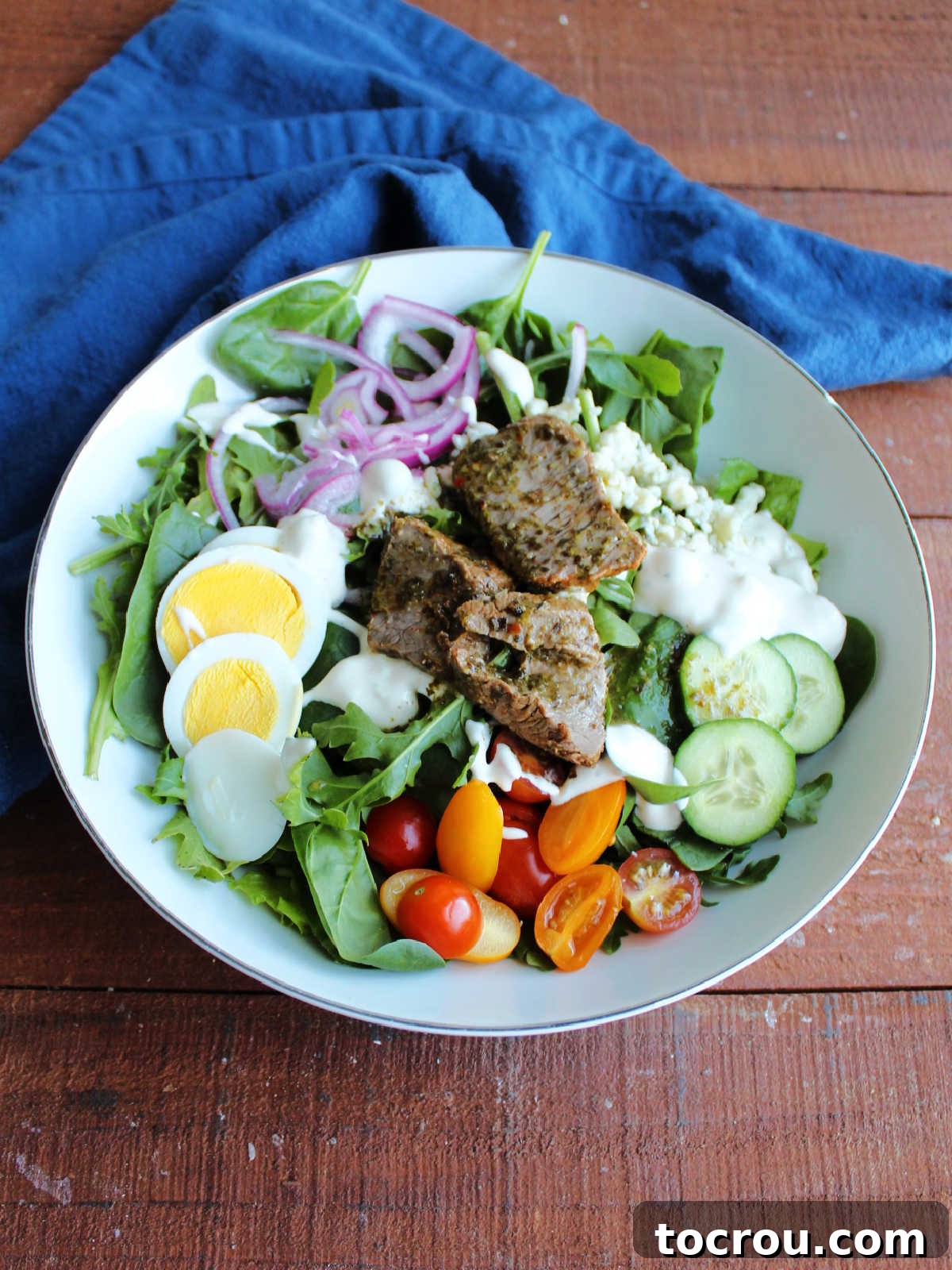 Fiercely Seared Rare Steak Salad 5 Single serving sized bowl filled with steak salad with blue cheese dressing and chimichurri sauce, ready to be eaten.