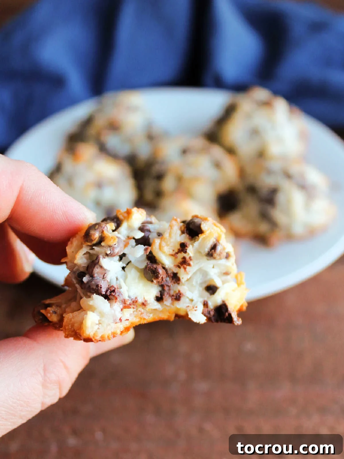 Maw-Maw's Delightful Almond Joy Macaroons 3 Hand holding an almond joy macaroon with a bite missing showing the soft texture of the interior with chocolate chips throughout the coconut cookie.