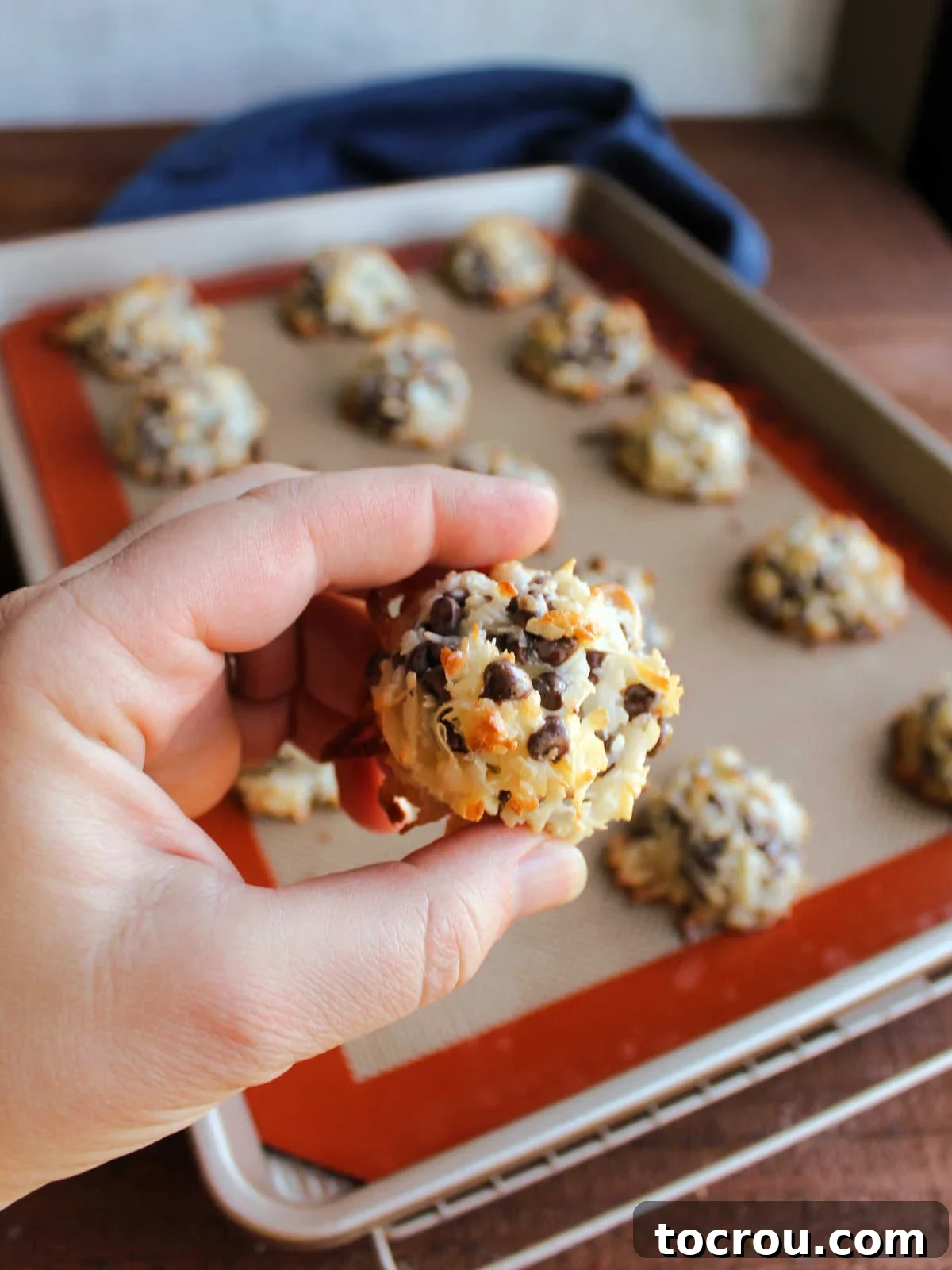 Maw-Maw's Delightful Almond Joy Macaroons 9 Hand holding baked almond joy cookie showing golden coconut edges and bits of chocolate inside.