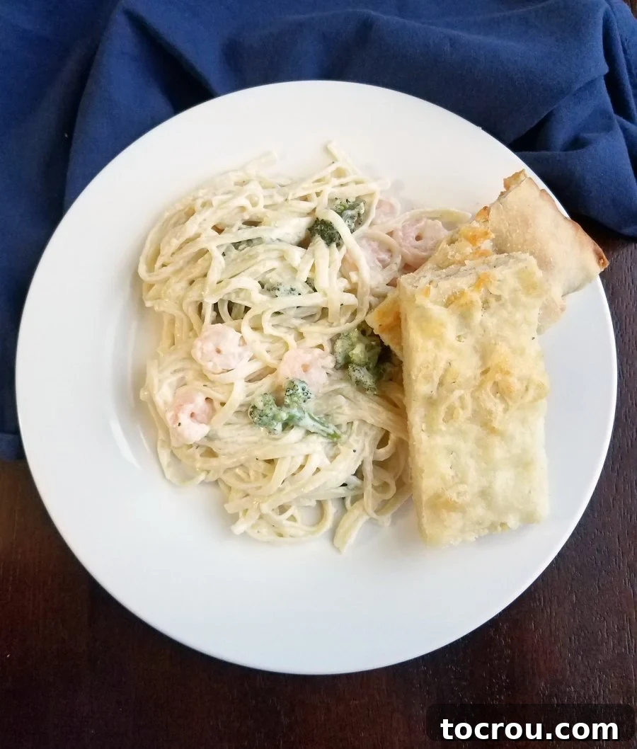 shrimp and broccoli fettuccine alfredo and slices of foccacia on plate.