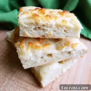 3 squares of cheesy garlic foccacia stacked on top of each other showing airy bread texture and golden brown cheese on top.