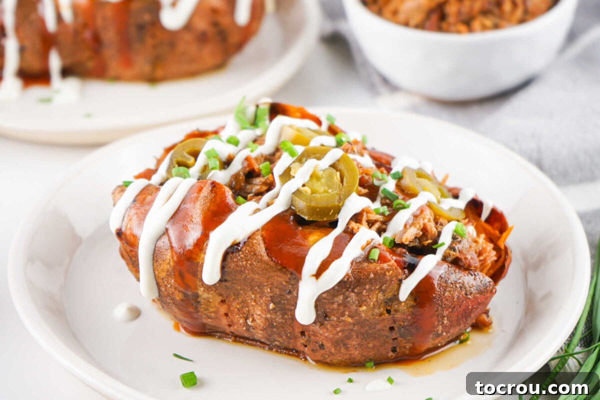 A vibrant plate featuring a pulled pork stuffed sweet potato, elegantly garnished with cool sour cream, tangy BBQ sauce, zesty jalapenos, and fresh chives, ready to be savored.