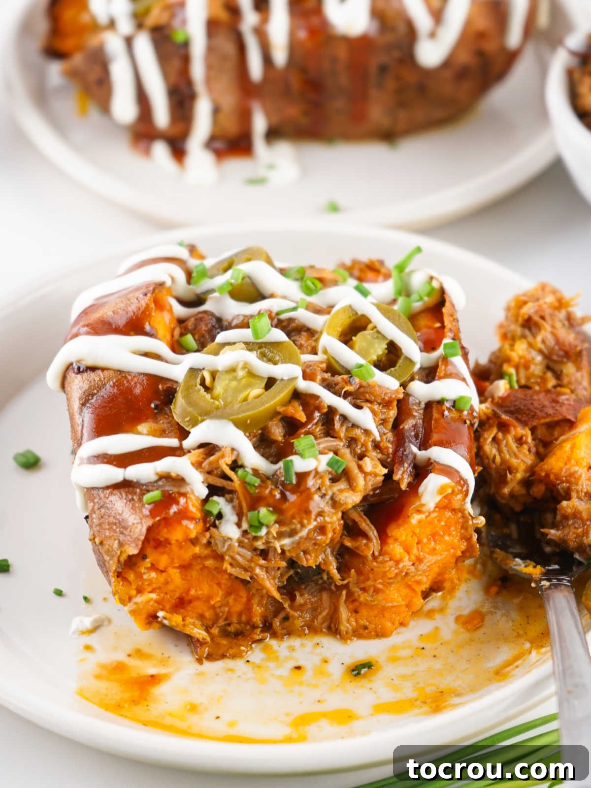A close-up view of a pulled pork sweet potato with a bite taken, revealing the vibrant orange interior of the sweet potato generously stuffed with rich BBQ pulled pork.