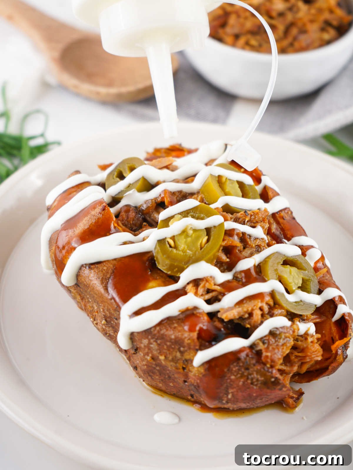 The finishing touch: a generous drizzle of cool, creamy sour cream cascading over the top of a warm, pulled pork stuffed sweet potato, adding a delightful contrast.