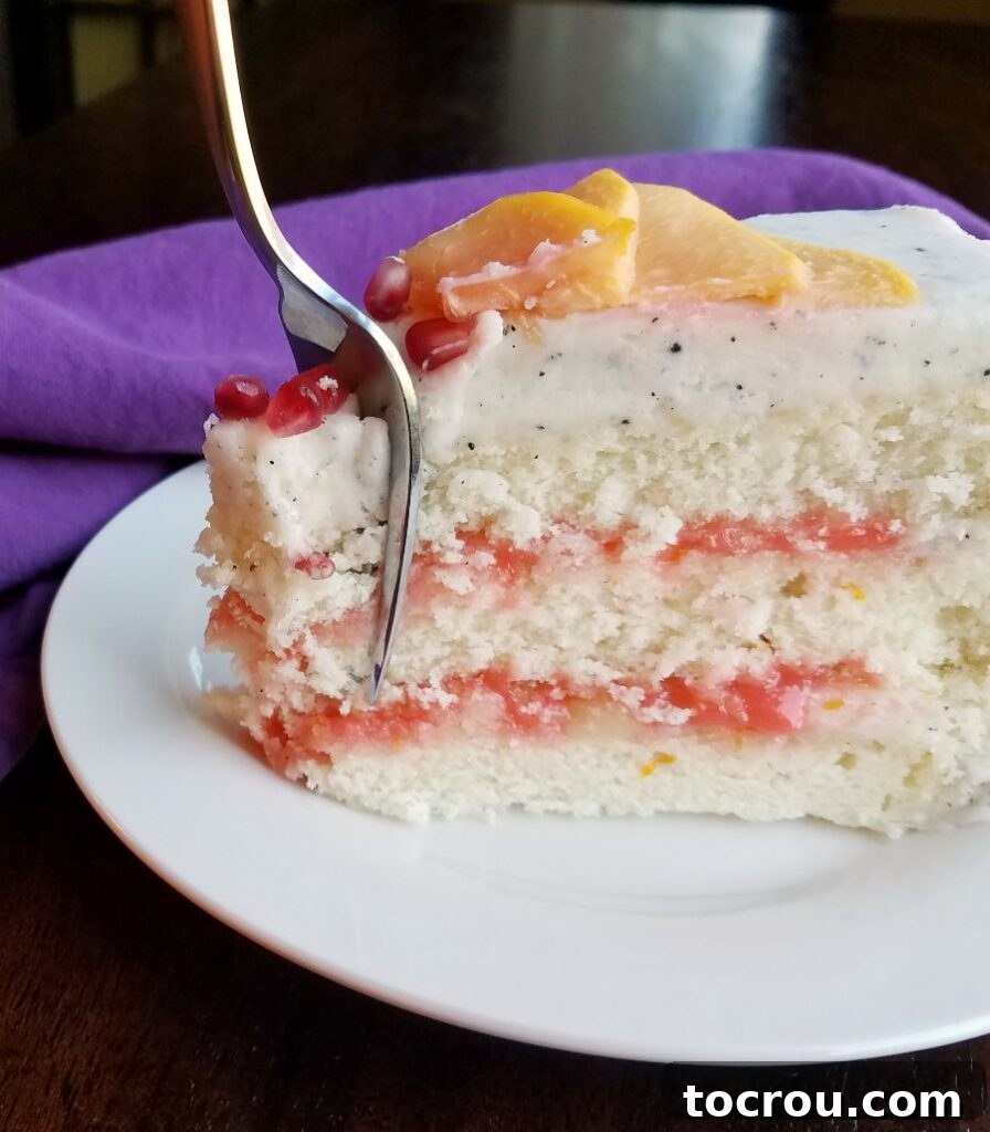 Close-up of a slice of layered white cake, showing pink blood orange curd and white frosting with black specks.