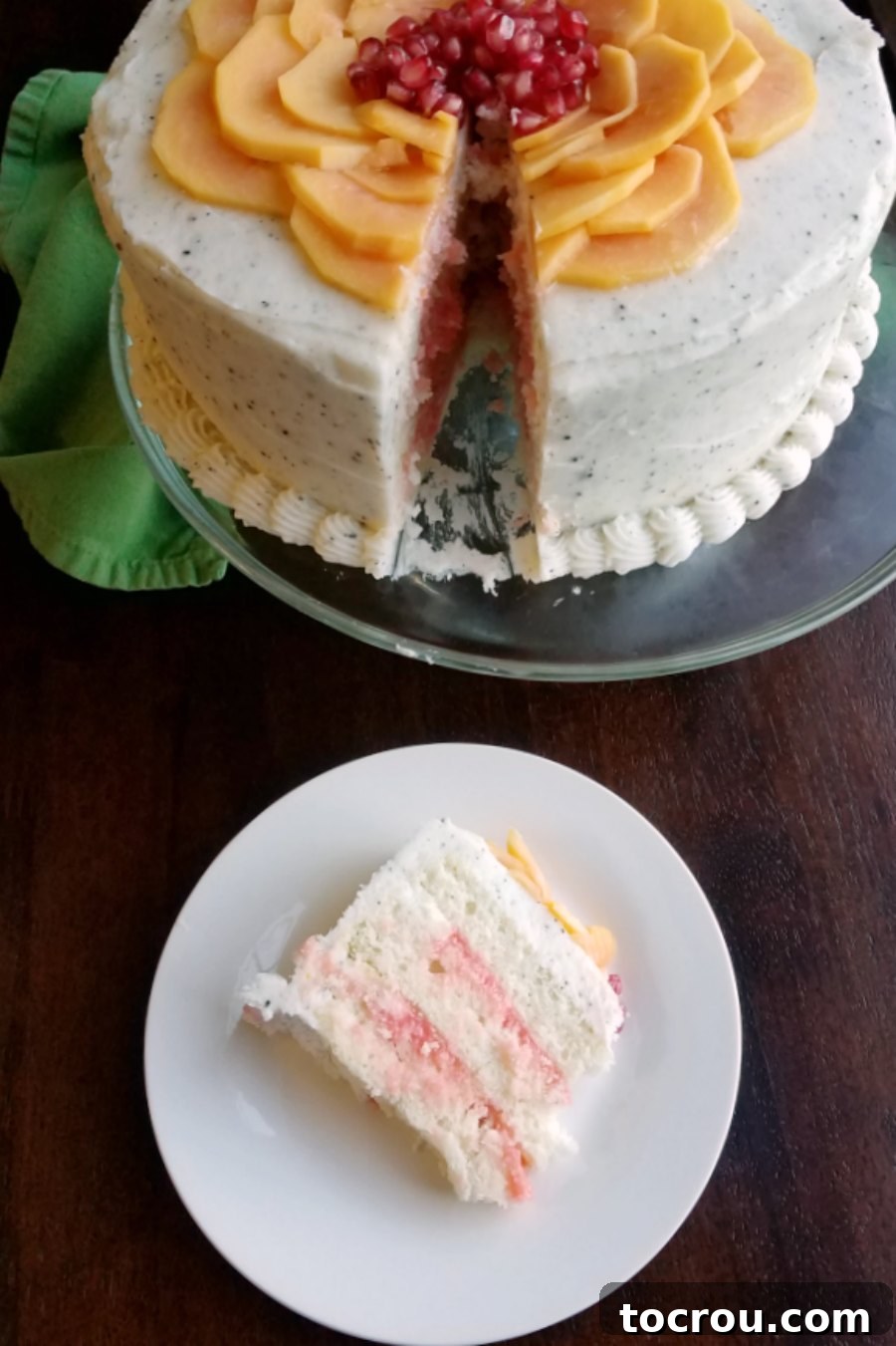 Slice of layered white cake with blood orange curd filling and dragonfruit buttercream on a plate, with the rest of the cake in the background.