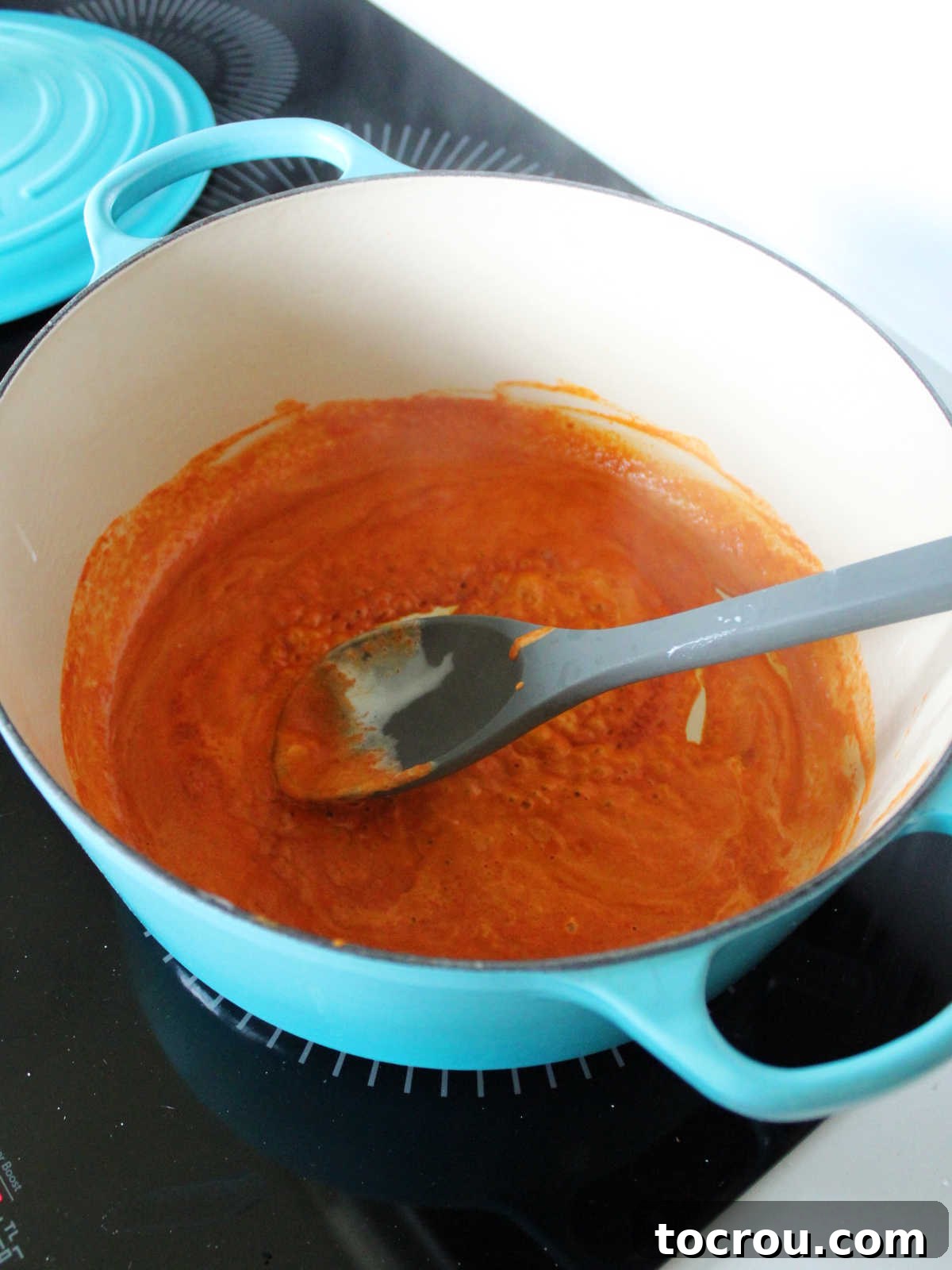 Red curry paste and thick coconut milk solids simmering in a large pot, releasing aromatic steam and vibrant colors as they cook down.