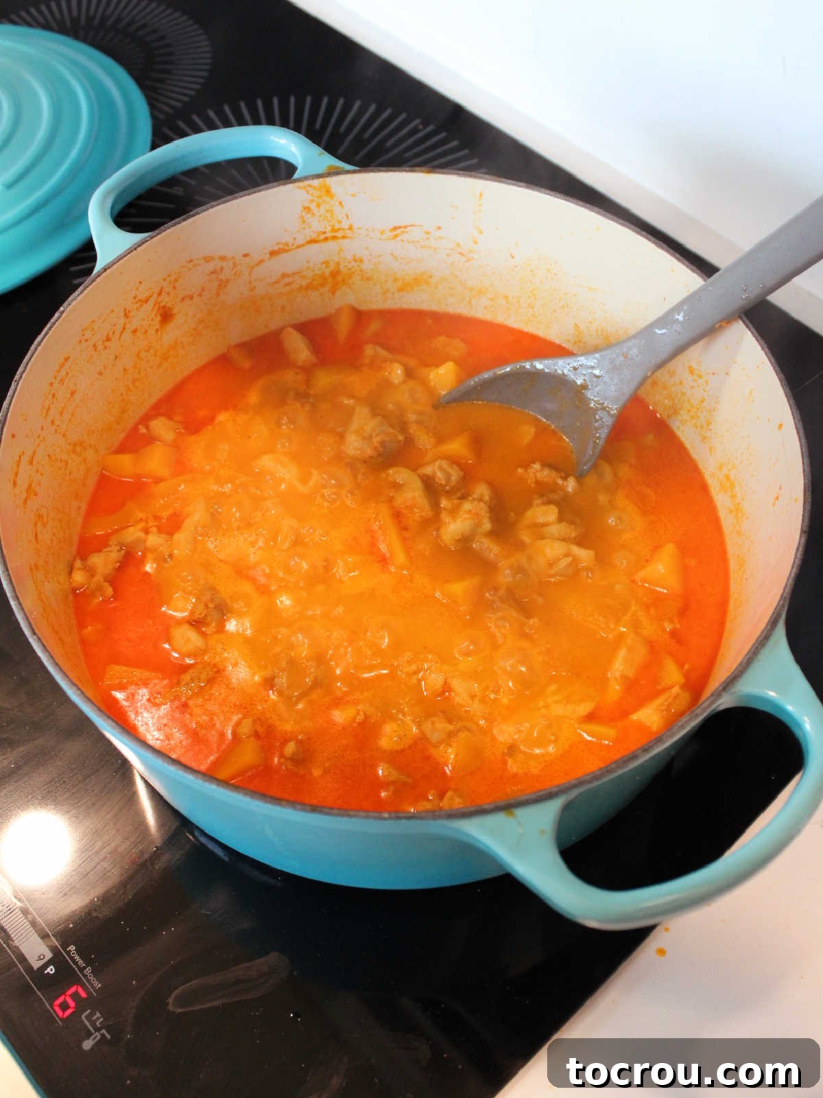 A large pot of rich red curry boiling gently on the stovetop, filled with chicken and vegetables, ready to be served.