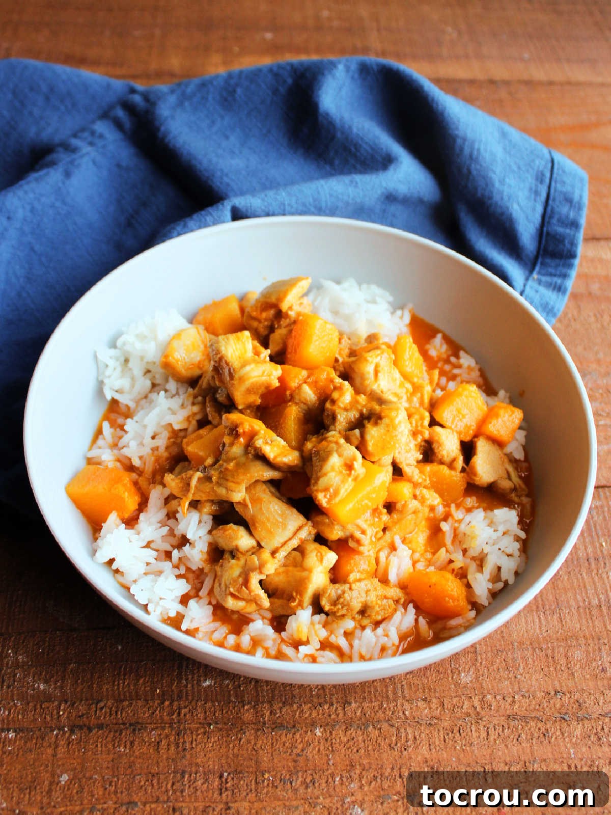 A close-up shot of a steaming bowl of Thai Red Curry Chicken with tender chicken pieces and vibrant butternut squash, served over fluffy white rice, ready to be enjoyed.