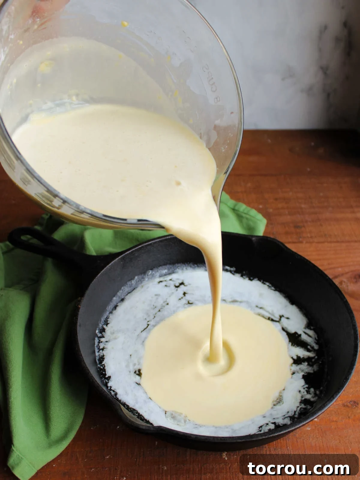 Mimi's Golden Custard Delight 5 Pouring german pancake batter into hot cast iron skillet that has bubbly melted butter inside.