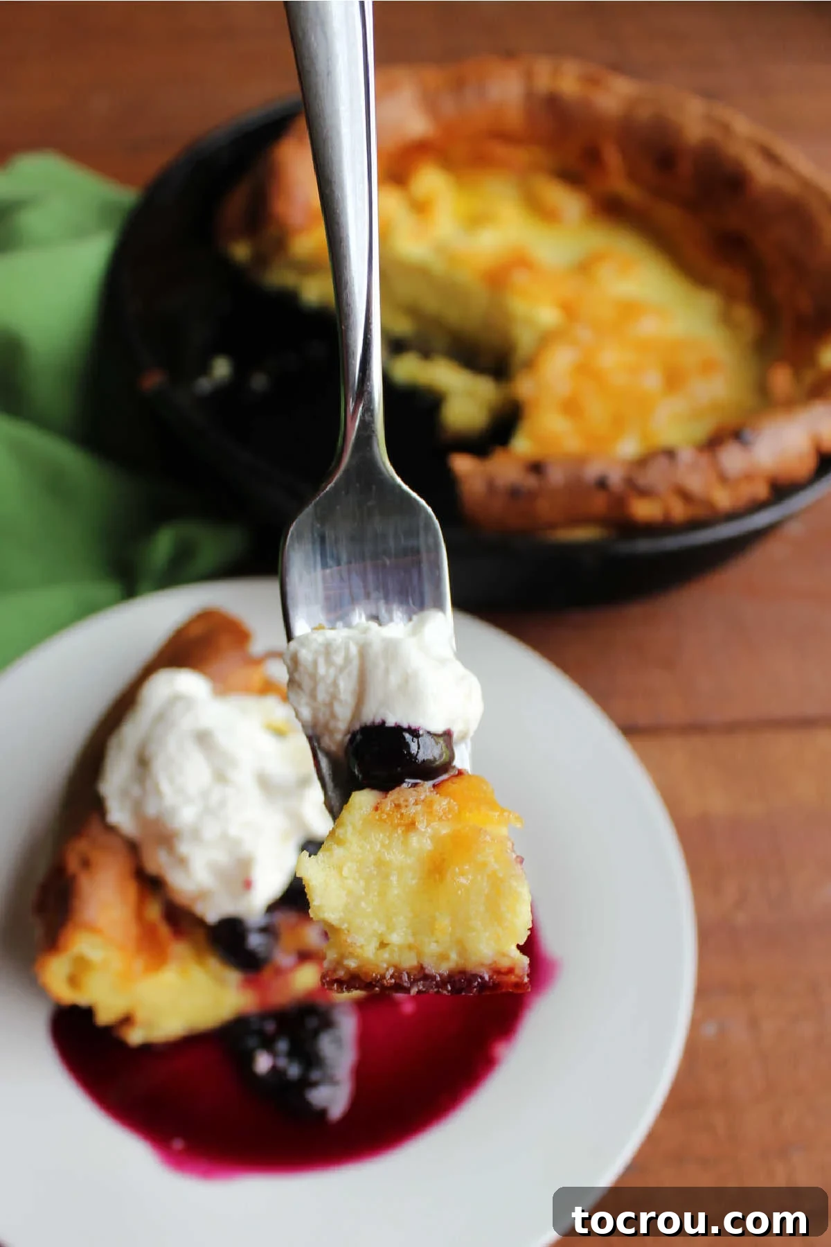 Mimi's Golden Custard Delight 8 Bite of custardy german pancake on fork with blueberry sauce and maple whipped cream.
