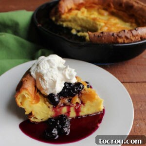 Slice of dutch baby pancake topped with blueberry syrup and maple whipped cream.