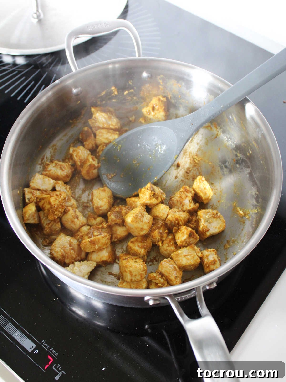 Stainless steel pan with chunks of browned chicken coated in curry powder, ginger, and turmeric. 