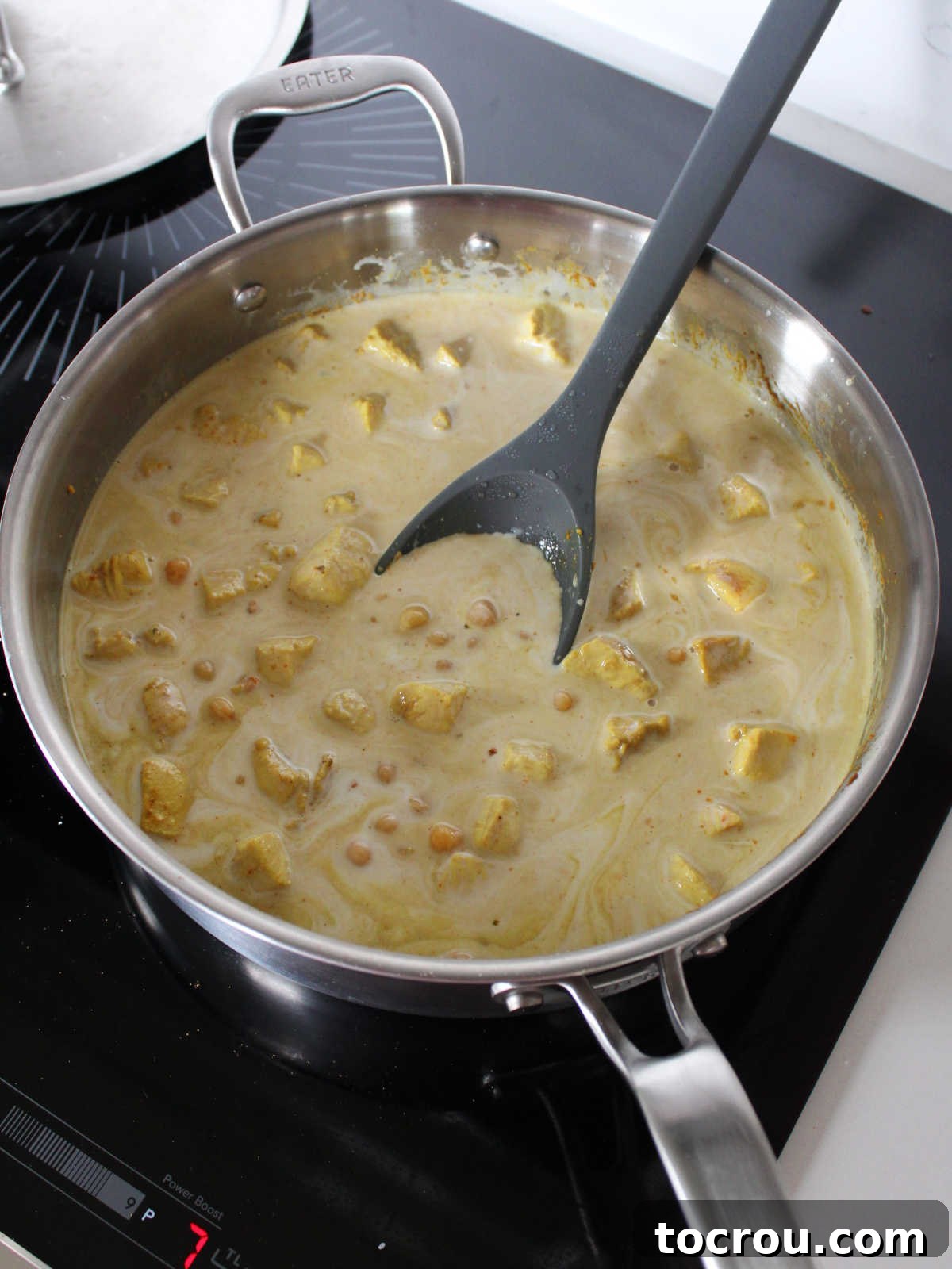 Chicken and chickpeas in pale yellow coconut milk broth, simmering.
