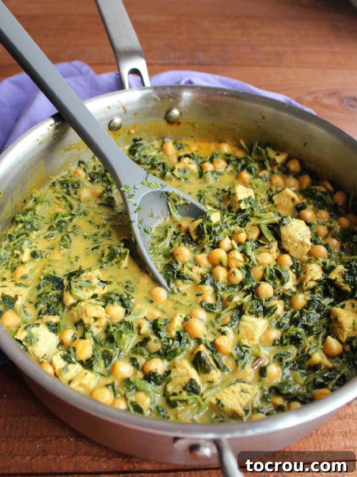 Pan of chicken and chickpea curry with yellow coconut milk broth and cooked spinach, ready to be served.
