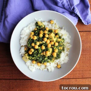 Bowl with jasmine rice topped with chicken and chickpea curry with yellow coconut milk broth and spinach.