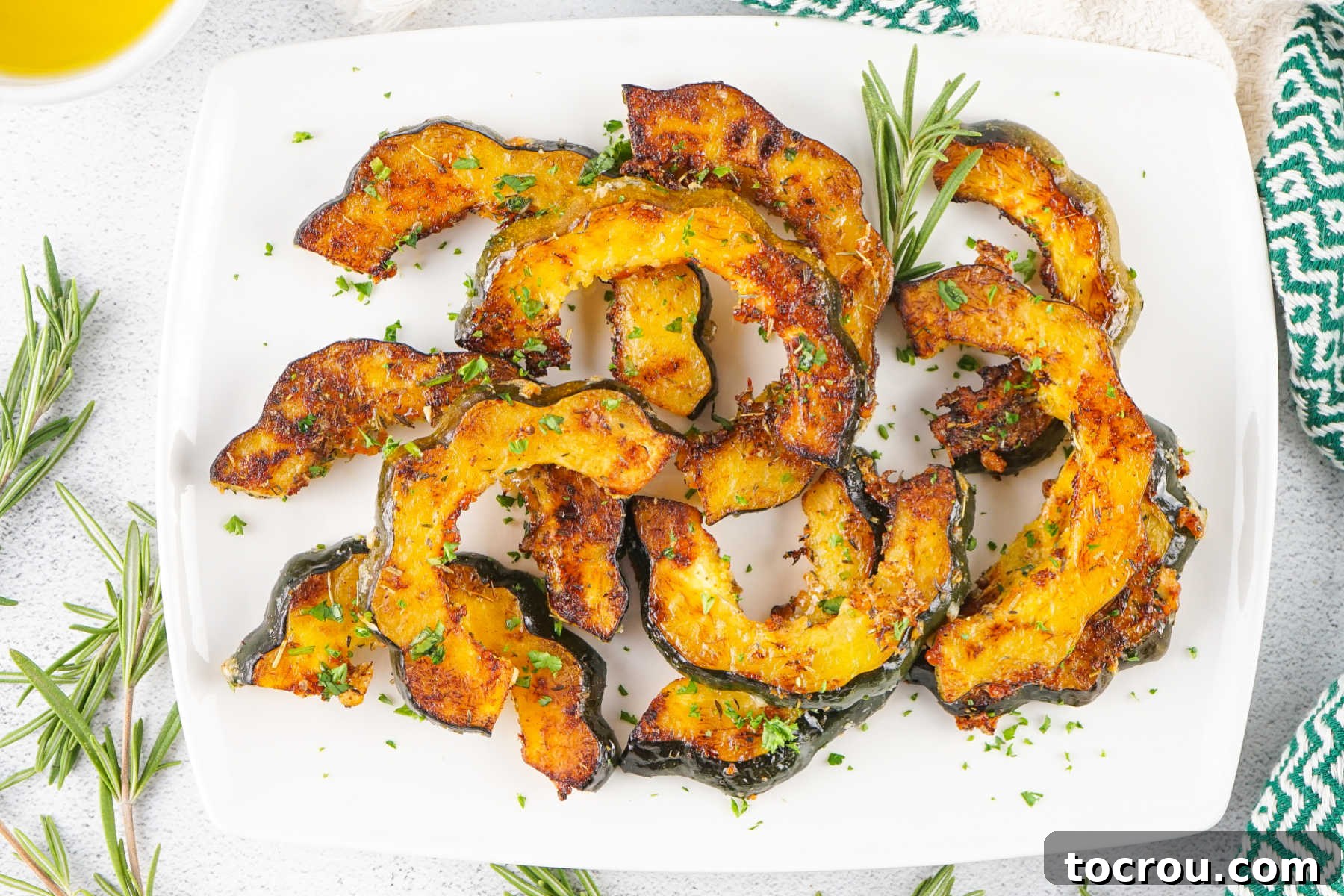 Platter with roasted acorn squash slices with bits of caramelized golden brown squash, herbs, and parmesan cheese. 