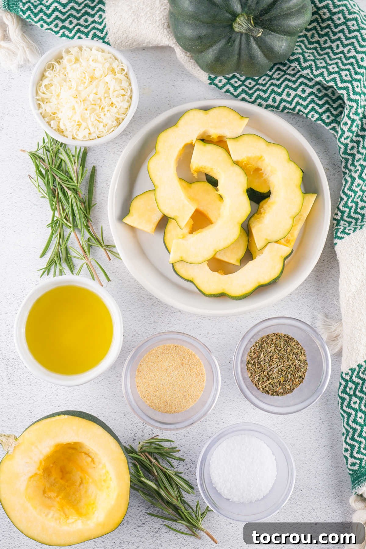 Ingredients including acorn squash, oil, garlic, rosemary, an herb mixture, and parmesan cheese. 