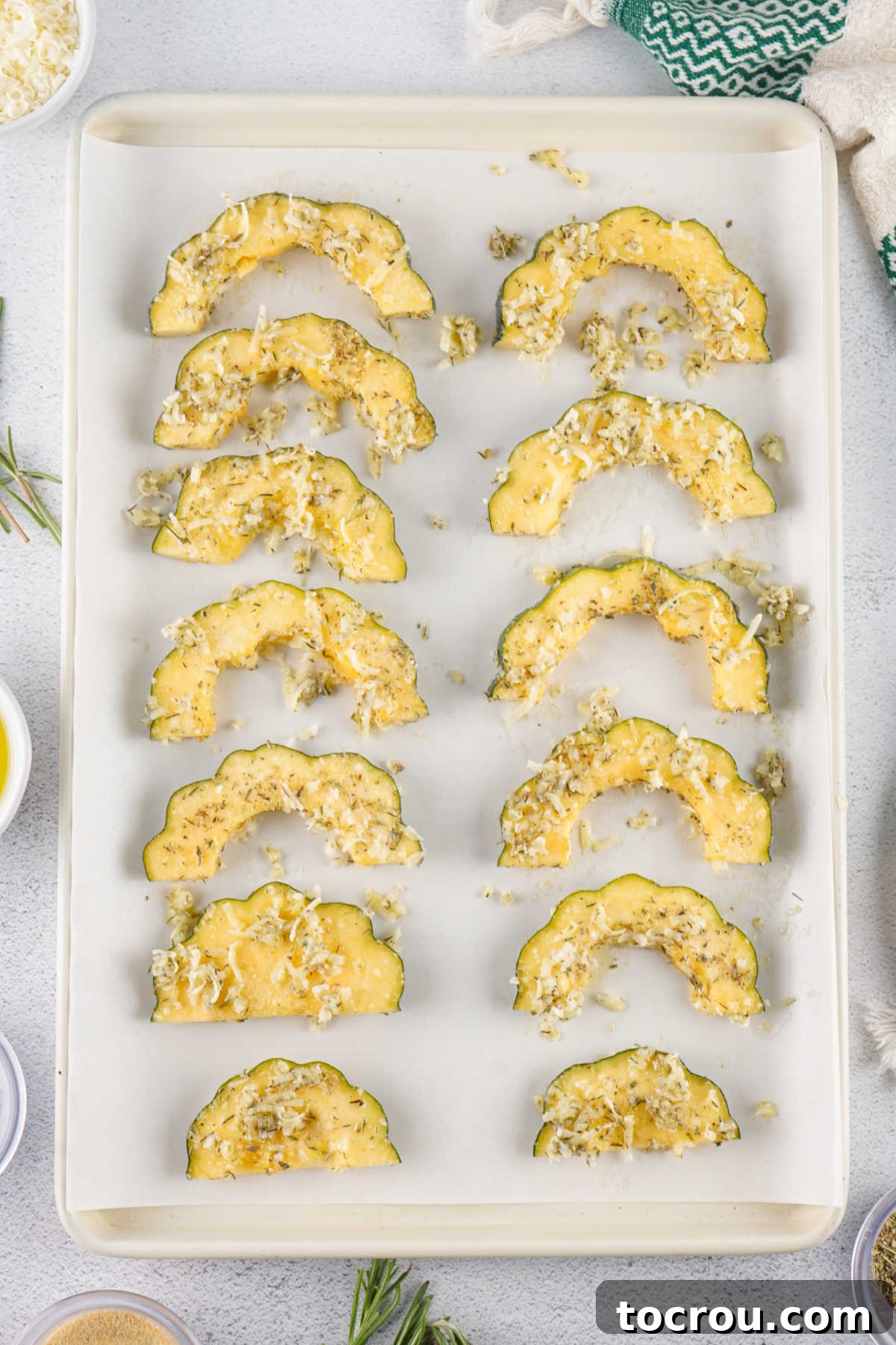 Sliced acorn squash coated in oil and seasonings on baking sheet ready to go in the oven. 