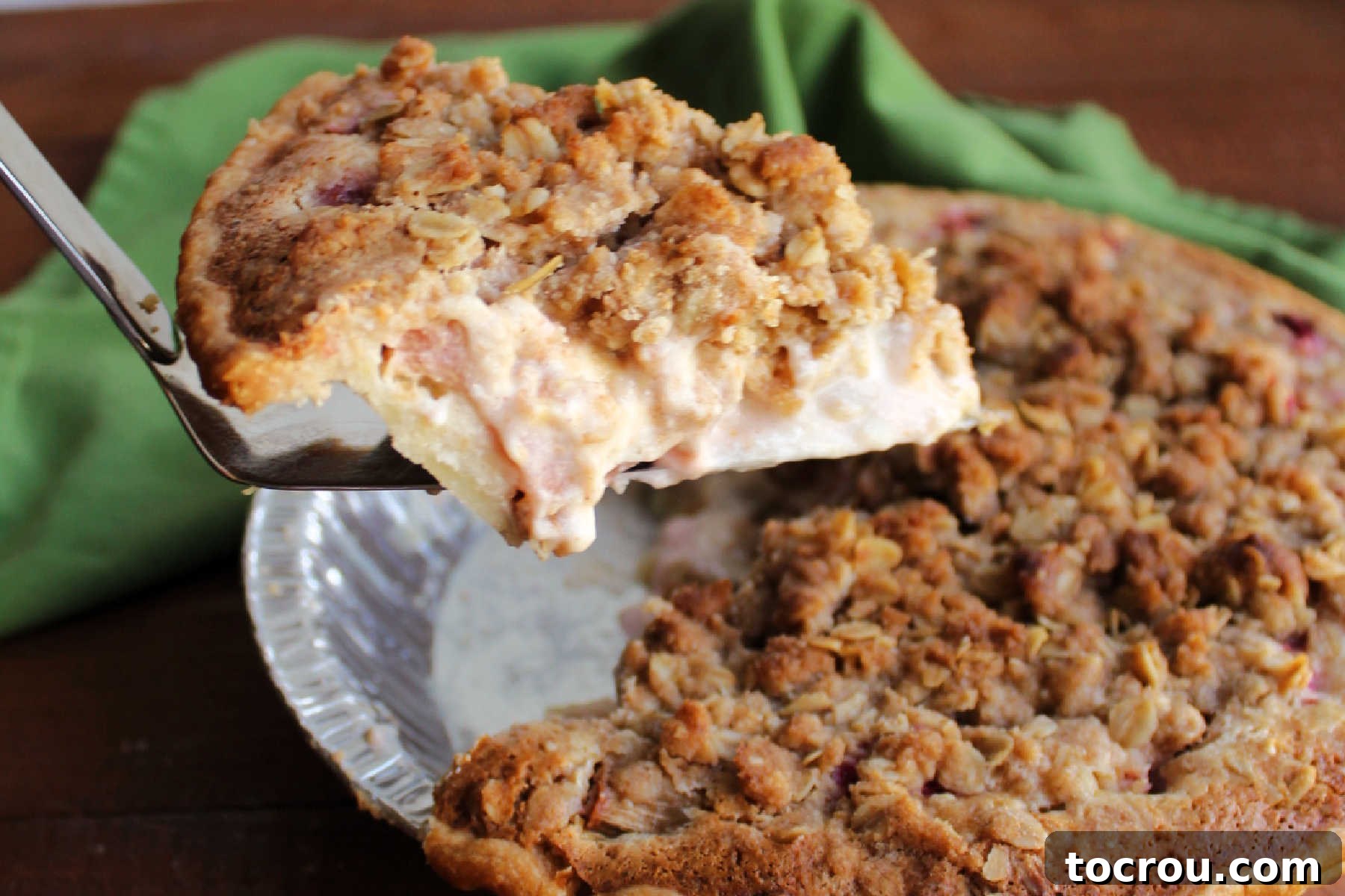 Pie serving lifting out slice of rhubarb pie with creamy sour cream filling and golden brown oat crumb topping.