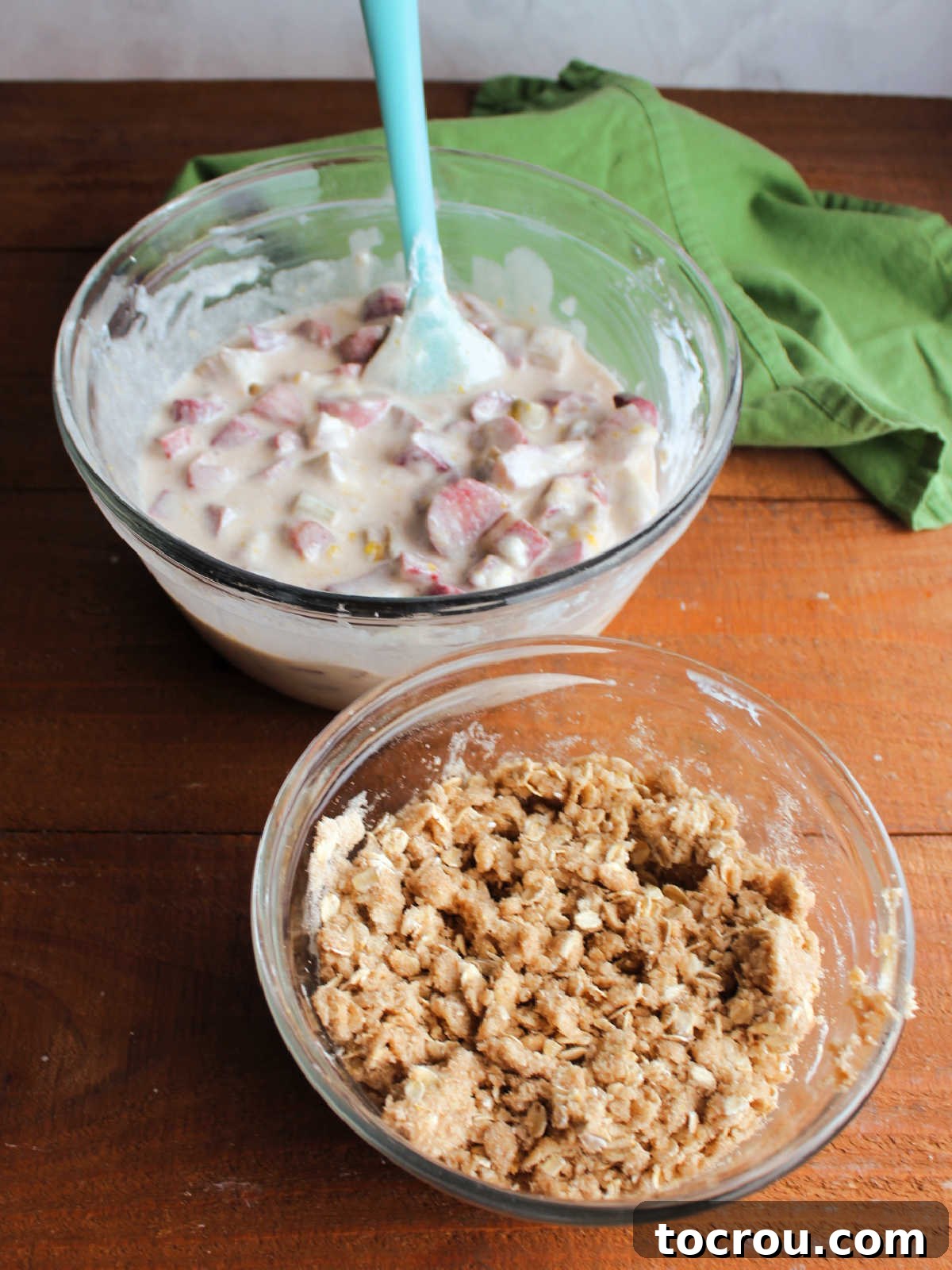 Mixing bowl with sour cream and rhubarb mixture next to a smaller mixing bowl with brown sugar and oatmeal crumb topping ingredients.