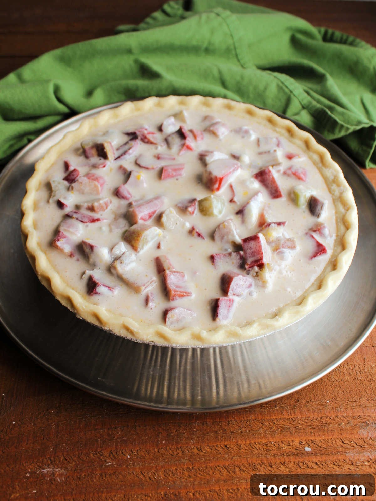 Creamy sour cream and rhubarb filling in raw pie crust, ready for crumb topping.