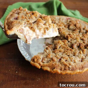 Lifting slice of sour cream rhubarb pie out of pan showing creamy filling and crunchy topping.