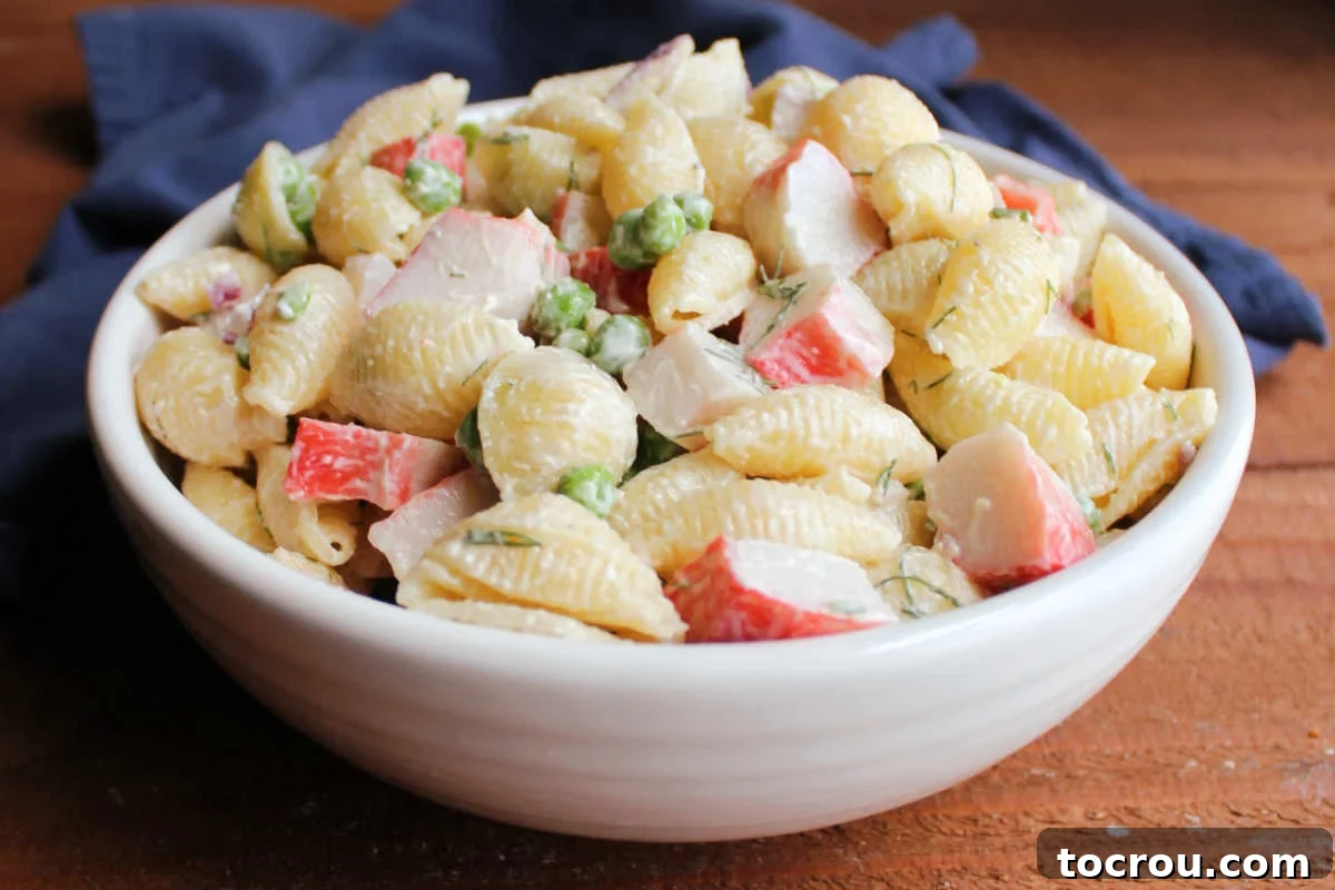 Bowl of imitation crab pasta salad with peas, red onions, shell pasta, and creamy dressing. 