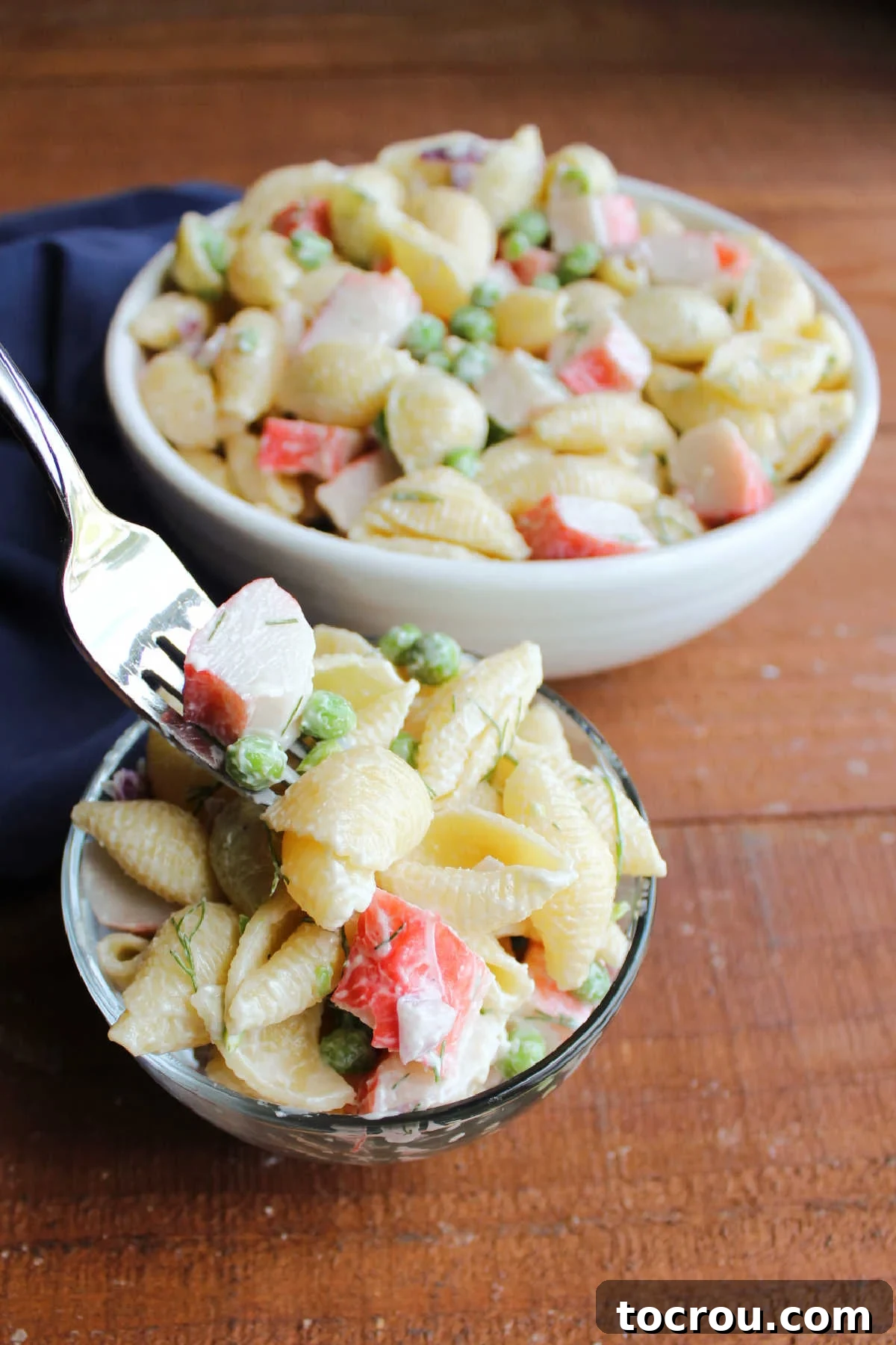 Forkful of crab macaroni salad with creamy dressing and peas, ready to eat. 