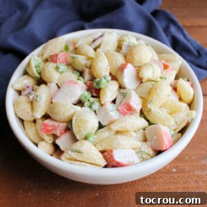 Serving bowl filled with crab pasta salad with chunks of imitation crab, shell pasta, peas, dill, and creamy mayonnaise dressing.