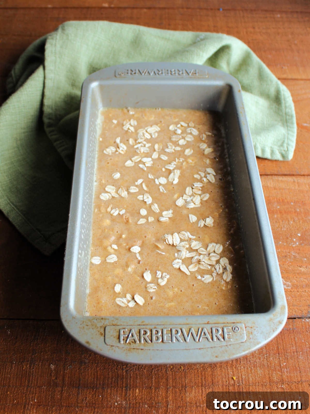 The applesauce oatmeal quick bread batter neatly poured into a greased loaf pan, with a delicate sprinkling of extra oats on top, patiently awaiting its transformation in the warm oven.