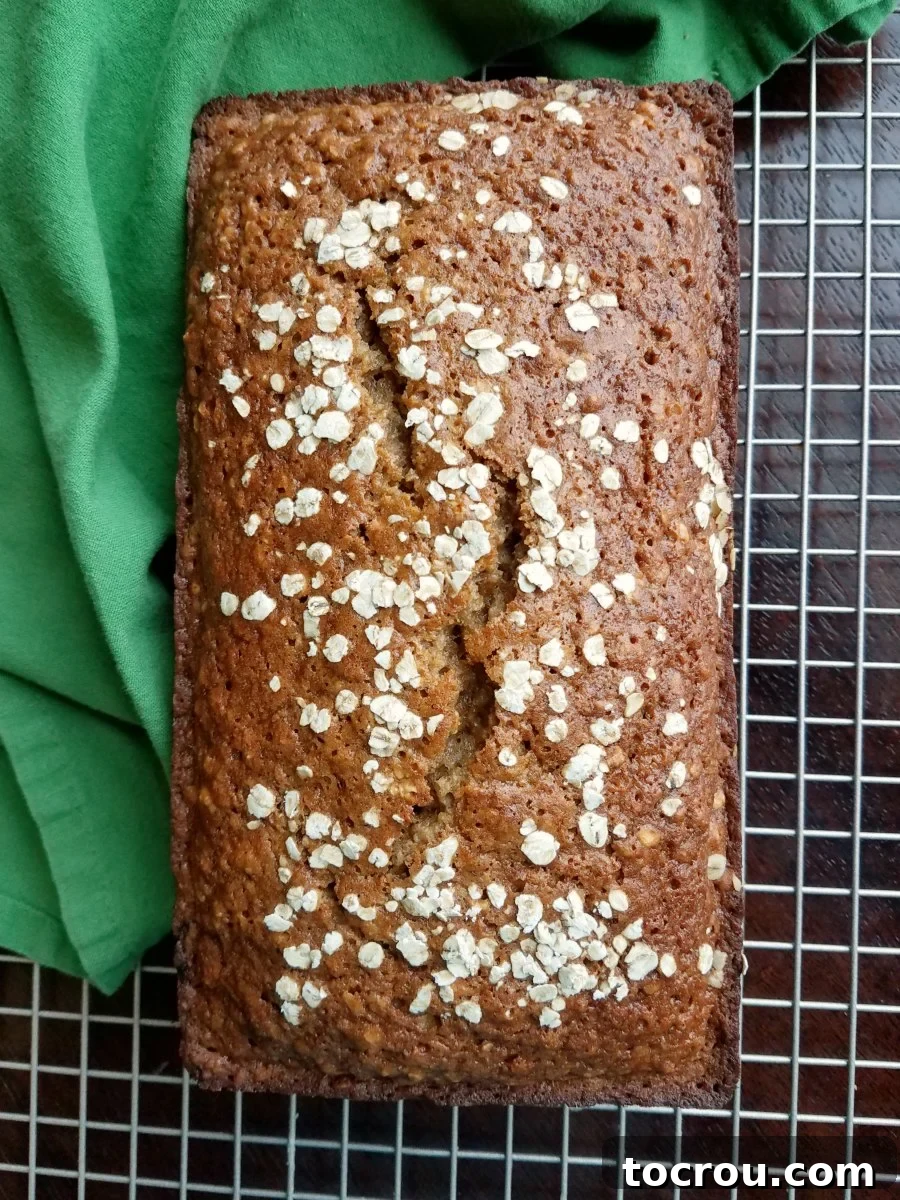 A whole loaf of golden-brown applesauce oatmeal bread, with a rustic sprinkling of extra oats on its crust, cooling gracefully on a wire rack, promising delicious slices.