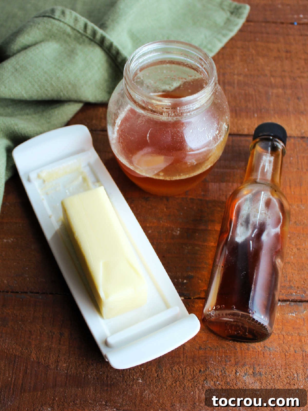 The simple, yet essential ingredients for vanilla honey butter: a golden stream of honey, a bottle of rich vanilla extract, and a stick of perfectly softened butter, all awaiting their delicious combination.